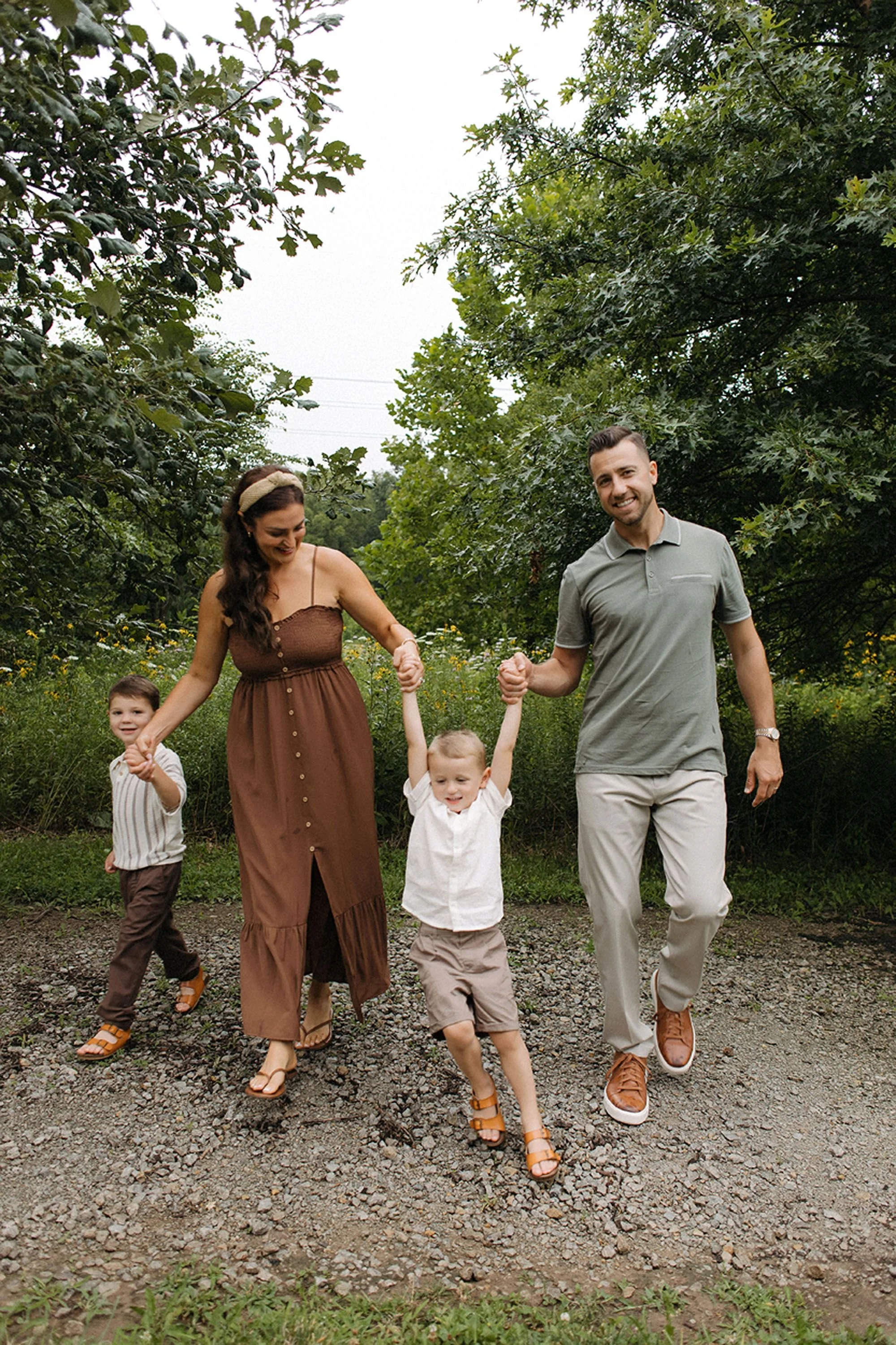 Parents holding hands with their two young sons while walking together on a garden path.