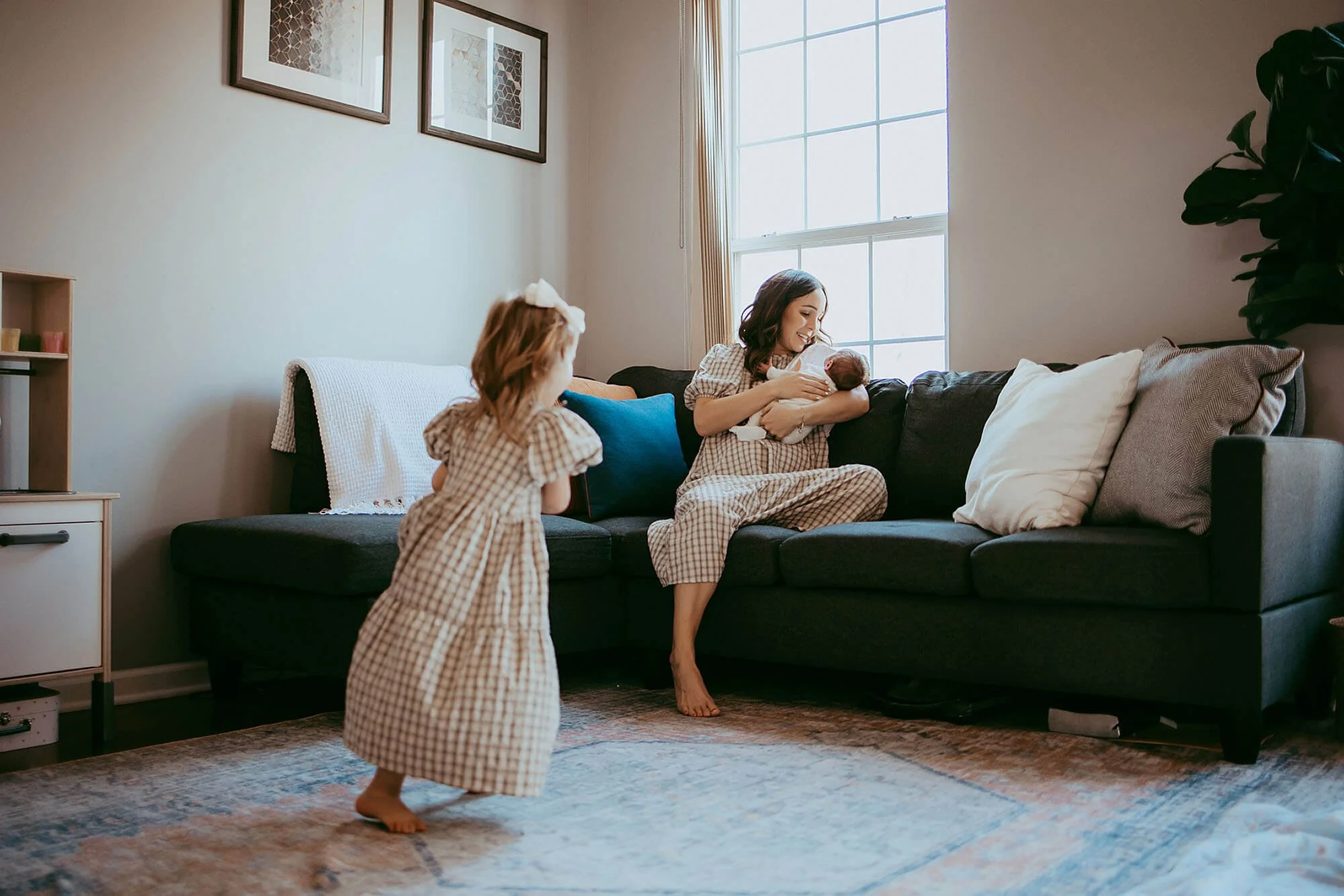 A mother and her young daughter relax on a couch in a living room, captured during a New Baby Photos session