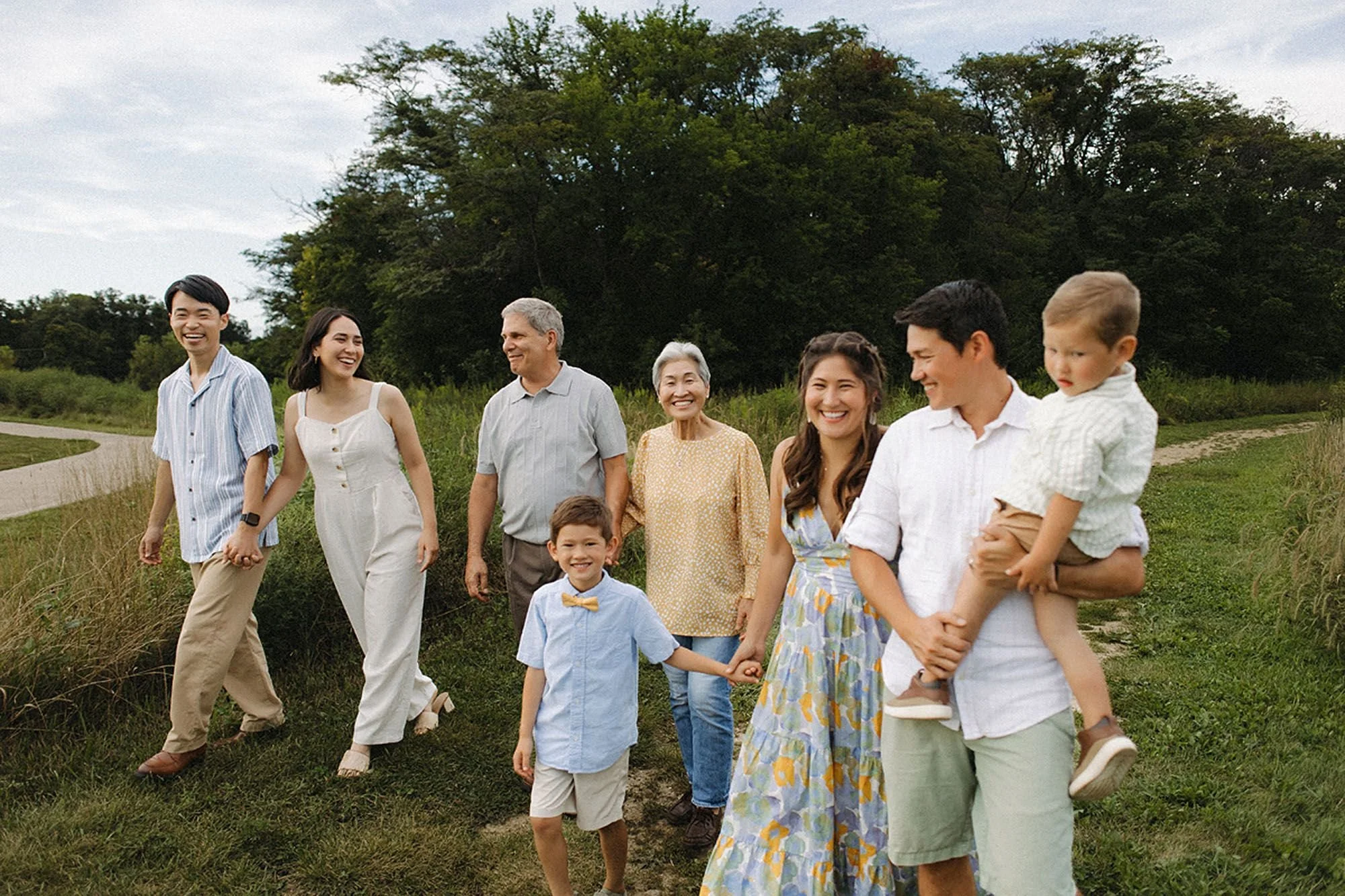 Multi-generational extended family walking together through a grassy field, smiling and holding hands, during a Flat Fork Creek Park family photo session