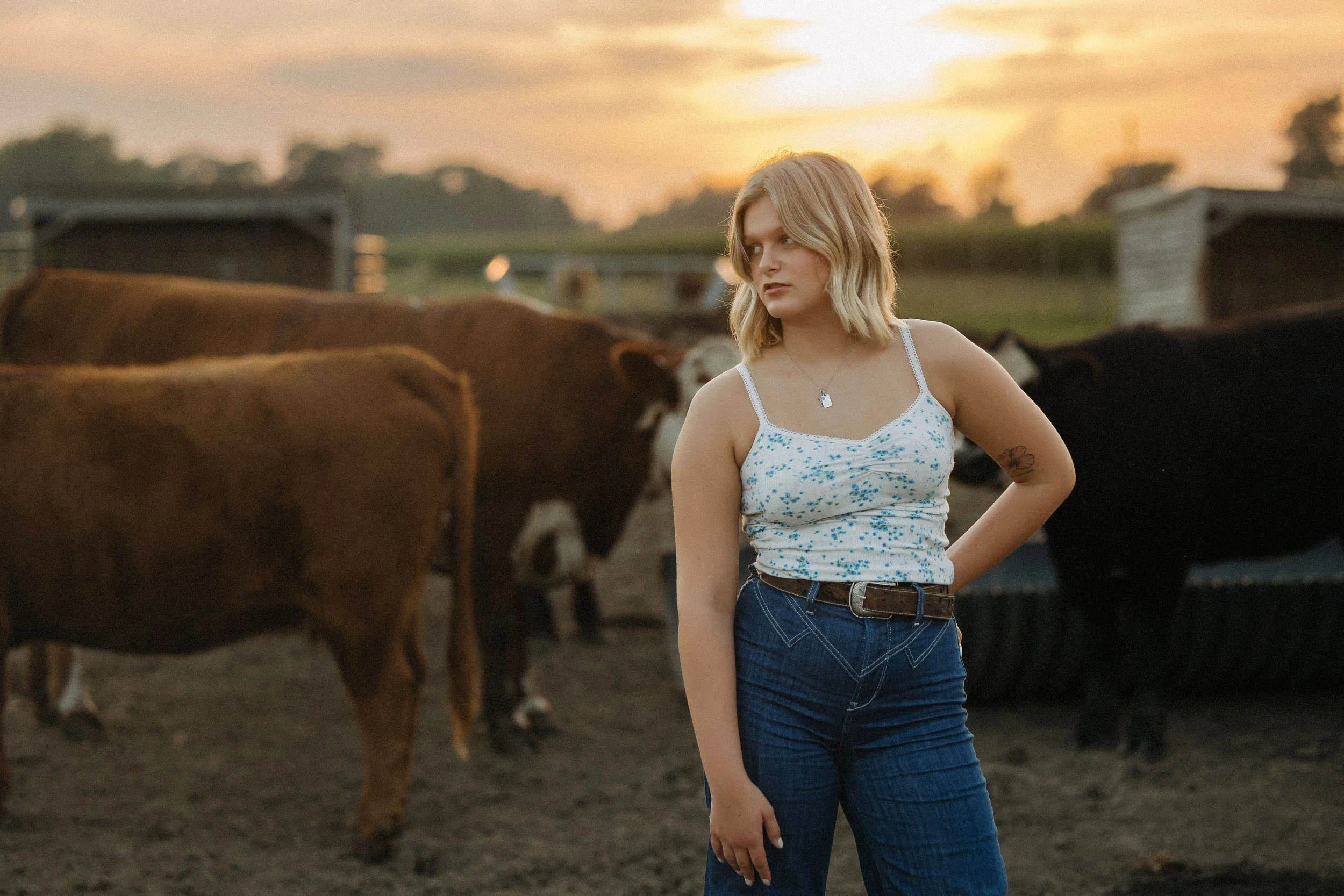 1. A woman in jeans stands in front of a group of cows in a rural setting.
