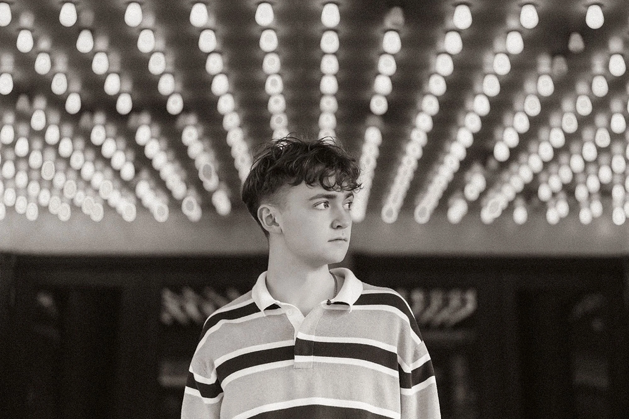 Black and white portrait of a high school senior beneath glowing marquee lights during a stylish, senior photo session Indianapolis
