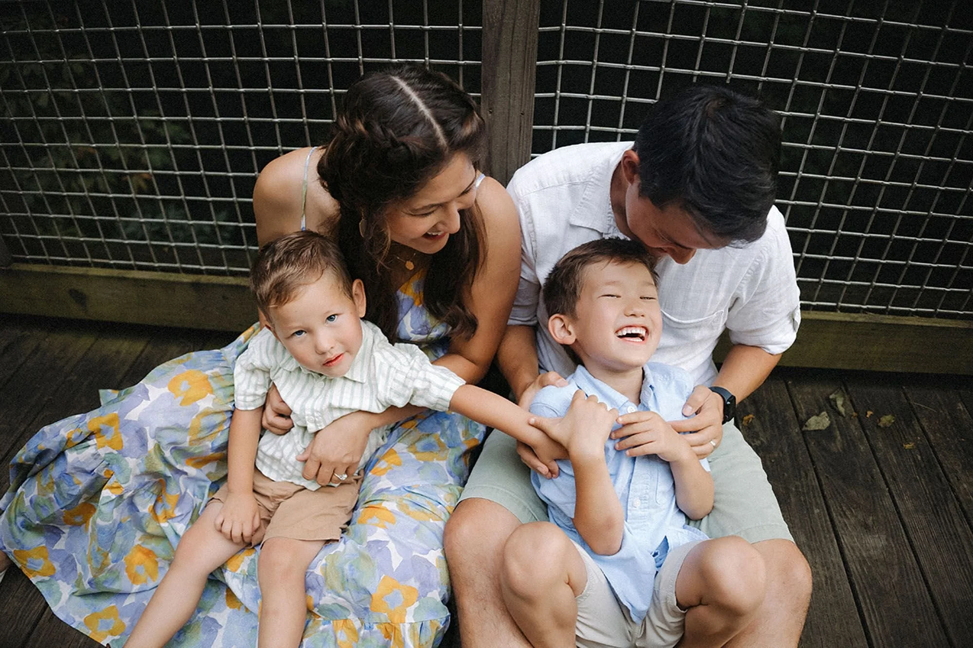 Extended family laughing together during a family photo session at Flat Fork Creek Park — parents cuddling two young sons on a wooden deck