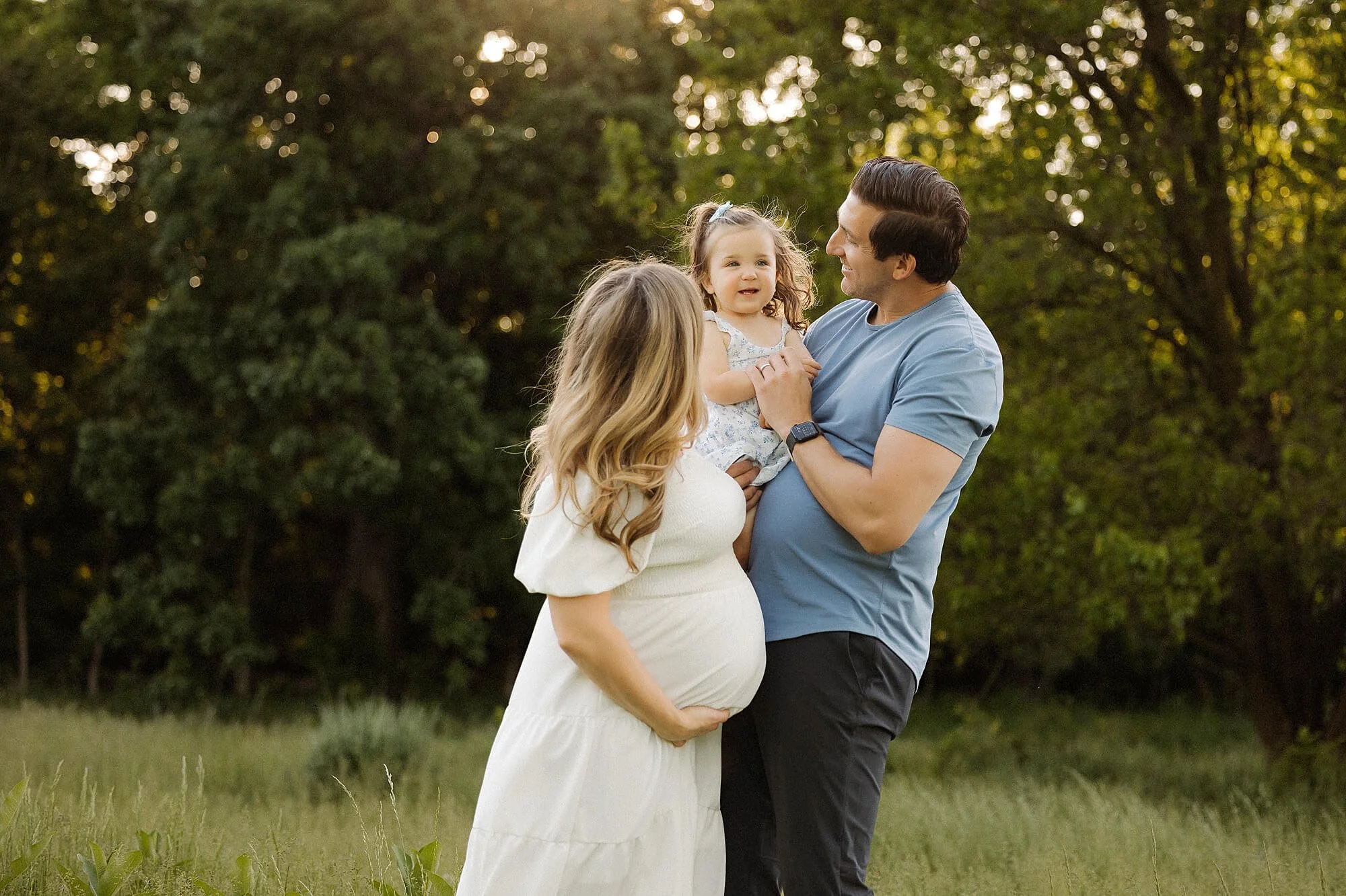 A cheerful family portrait taken in a park, featuring parents and children standing together amidst lush grass and trees.