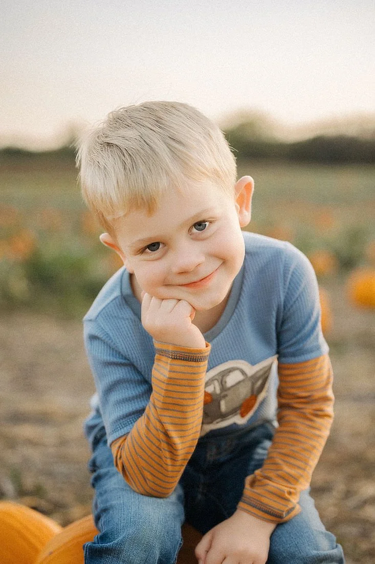 Young boy rests his chin on his hand and smiles softly during a cozy autumn portrait session at Dull’s Pumpkin Harvest.