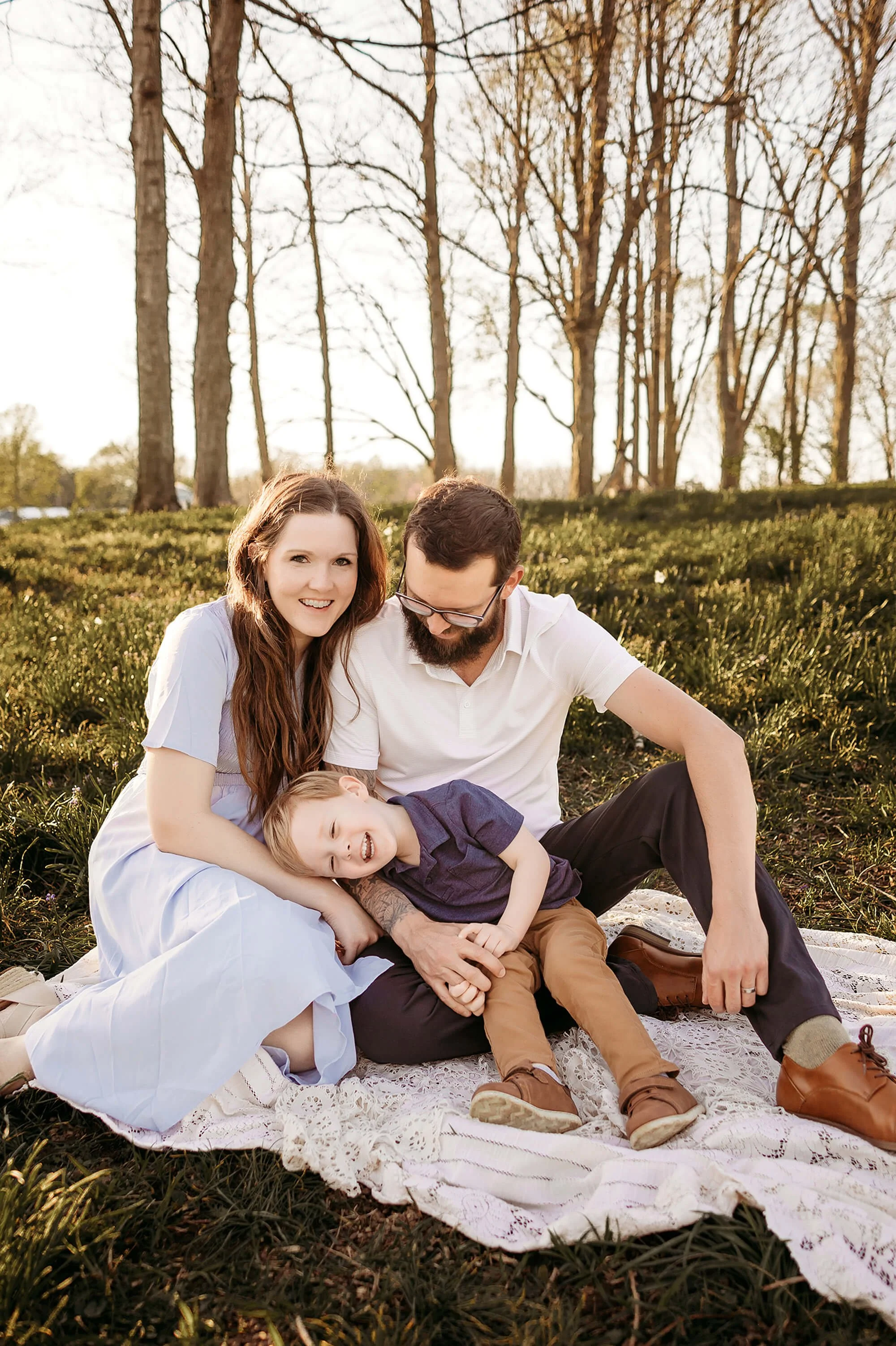 A smiling family stands on the grass, dressed in spring outfits, capturing a joyful moment in a photo.