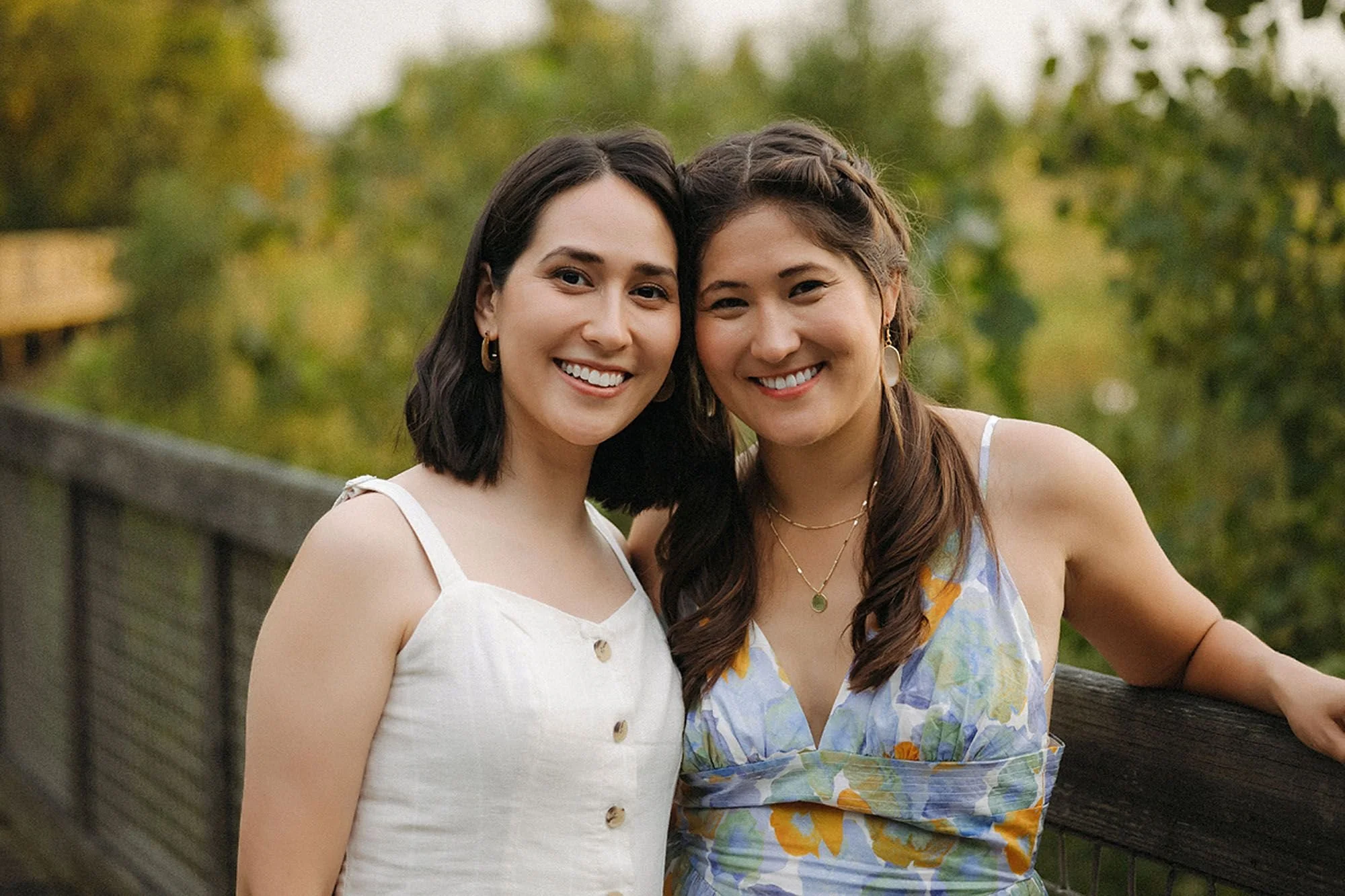 Flat Fork Creek Park Extended Family Photos Session featuring two smiling sisters sharing a warm embrace on a scenic boardwalk surrounded by lush greenery in Fishers, Indiana