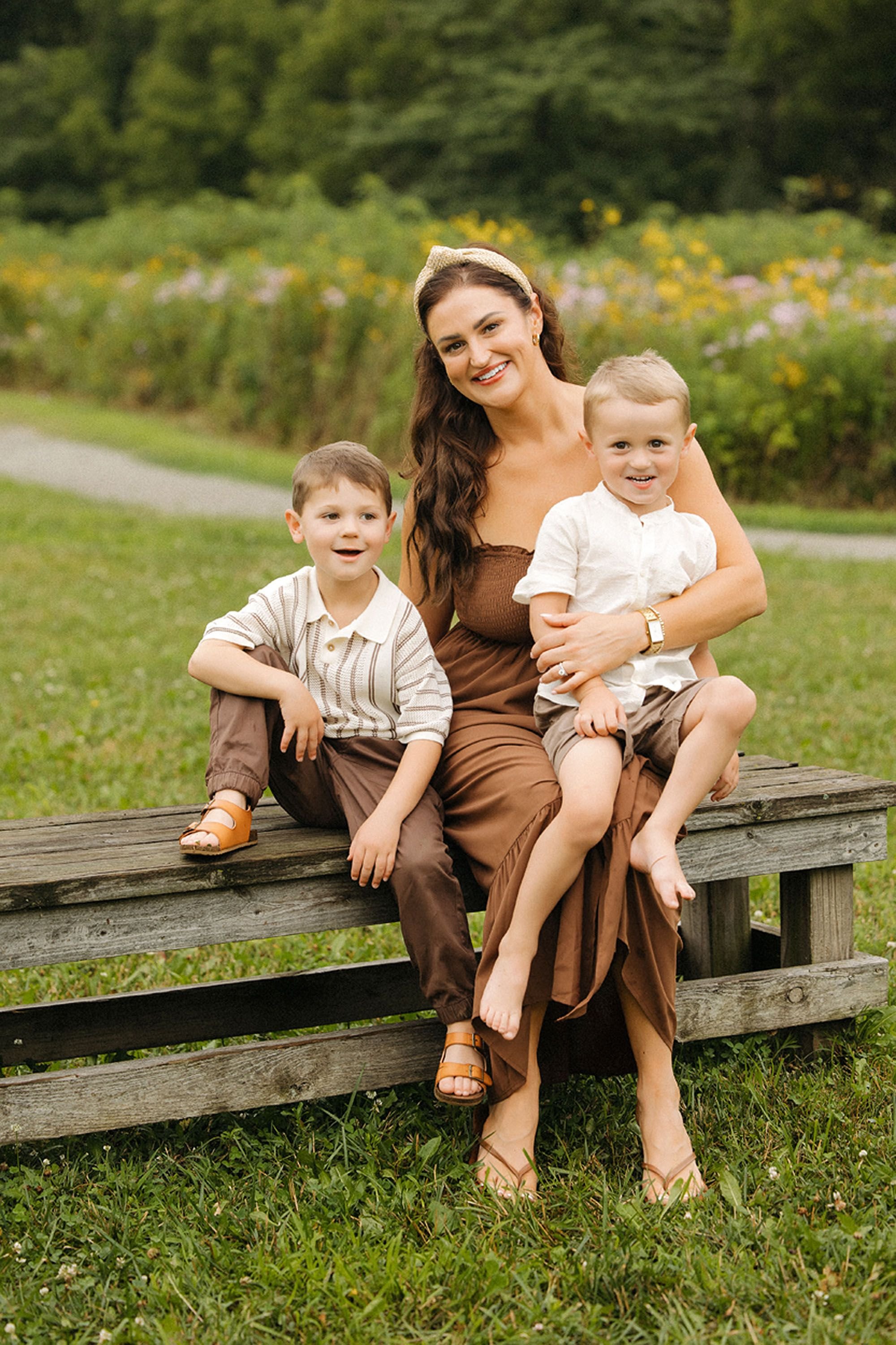 A mother sitting on a wooden bench with her two young sons during a summer family session.