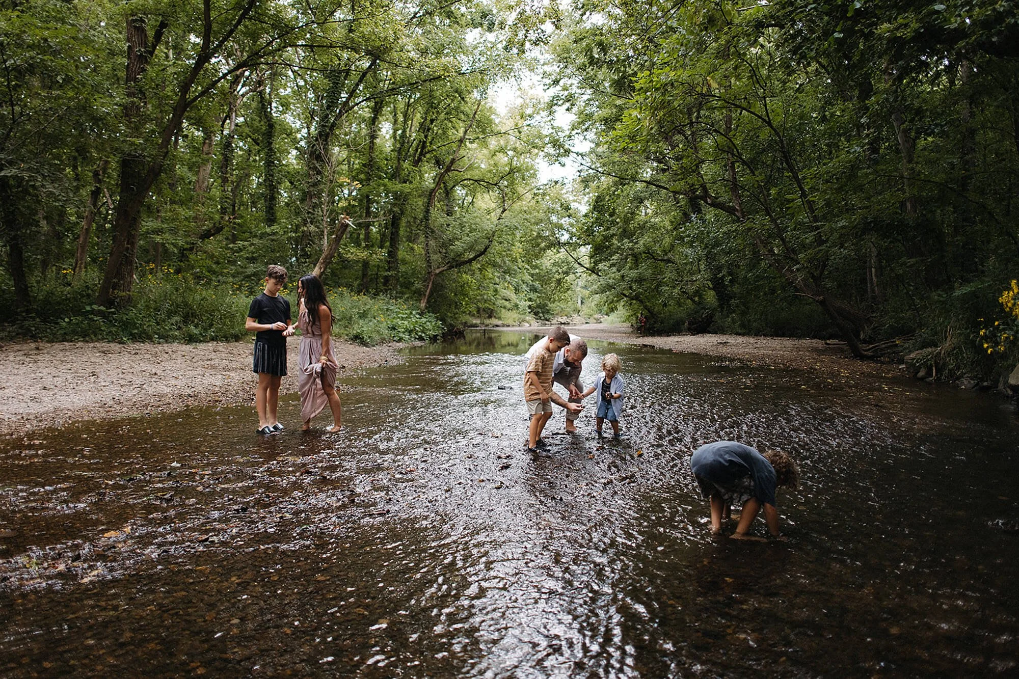 family members play together in a river at Flowing Well Park, Carmel, Indiana, with trees and water creating a serene backdrop