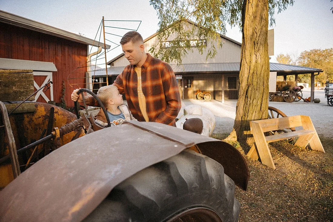 Father and young son explore an old tractor together near the rustic farm buildings during their fall visit to Dull’s Pumpkin Harvest