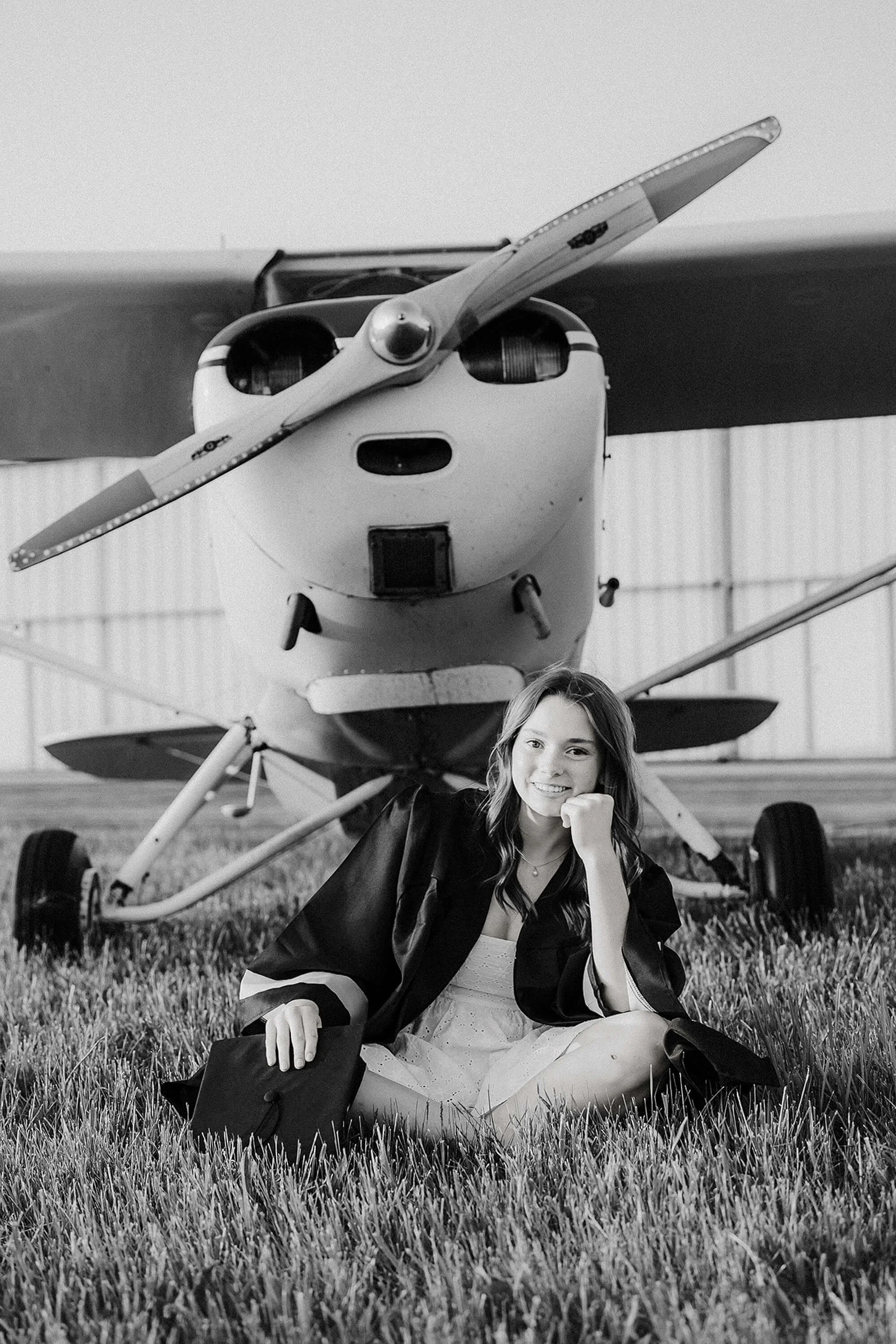 A woman is seated before an airplane, highlighting her senior photos against a backdrop of aviation