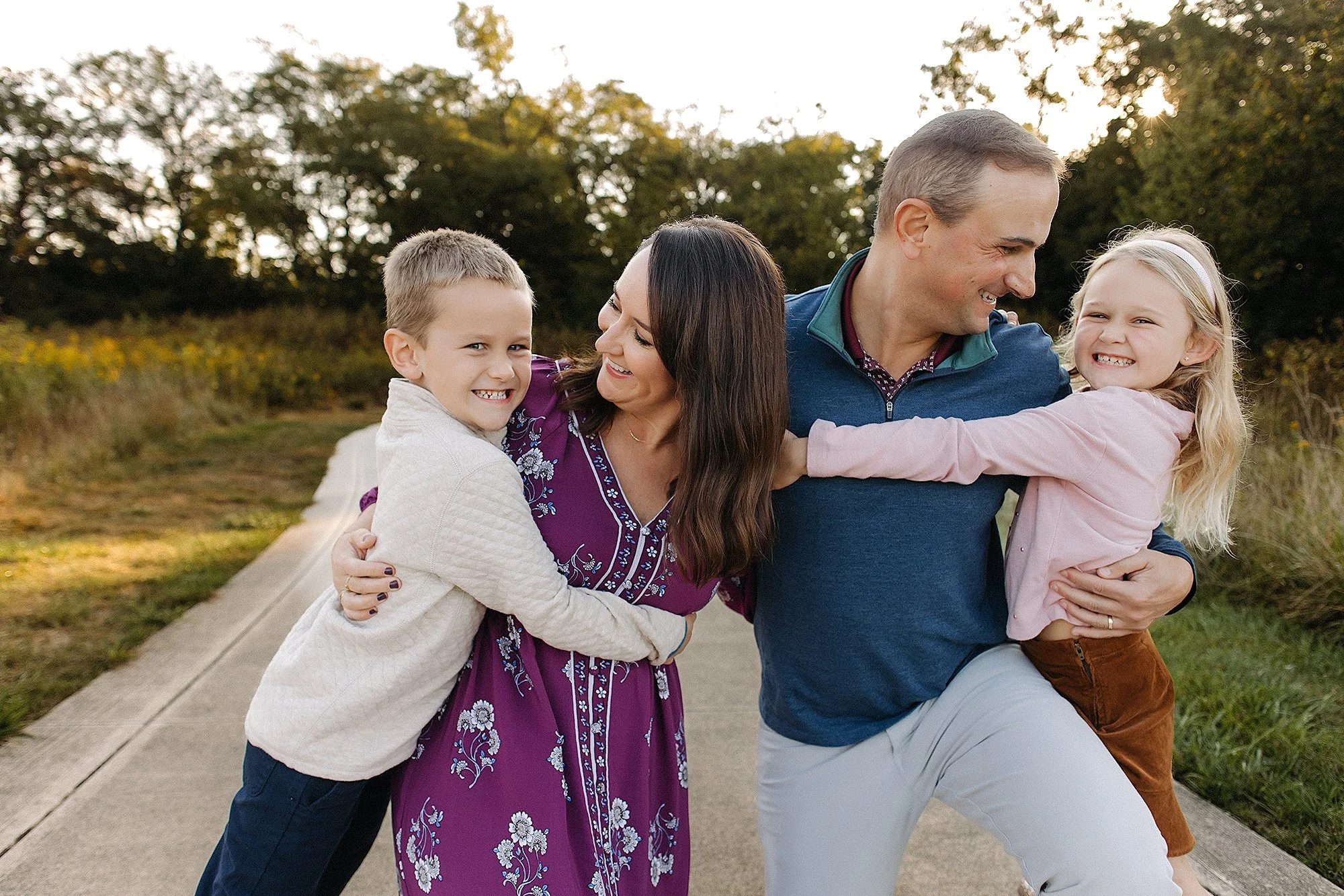 Happy family sharing playful hugs during an outdoor golden hour session, wearing coordinated fall outfits that inspire what to wear for family photos with timeless colors and effortless style