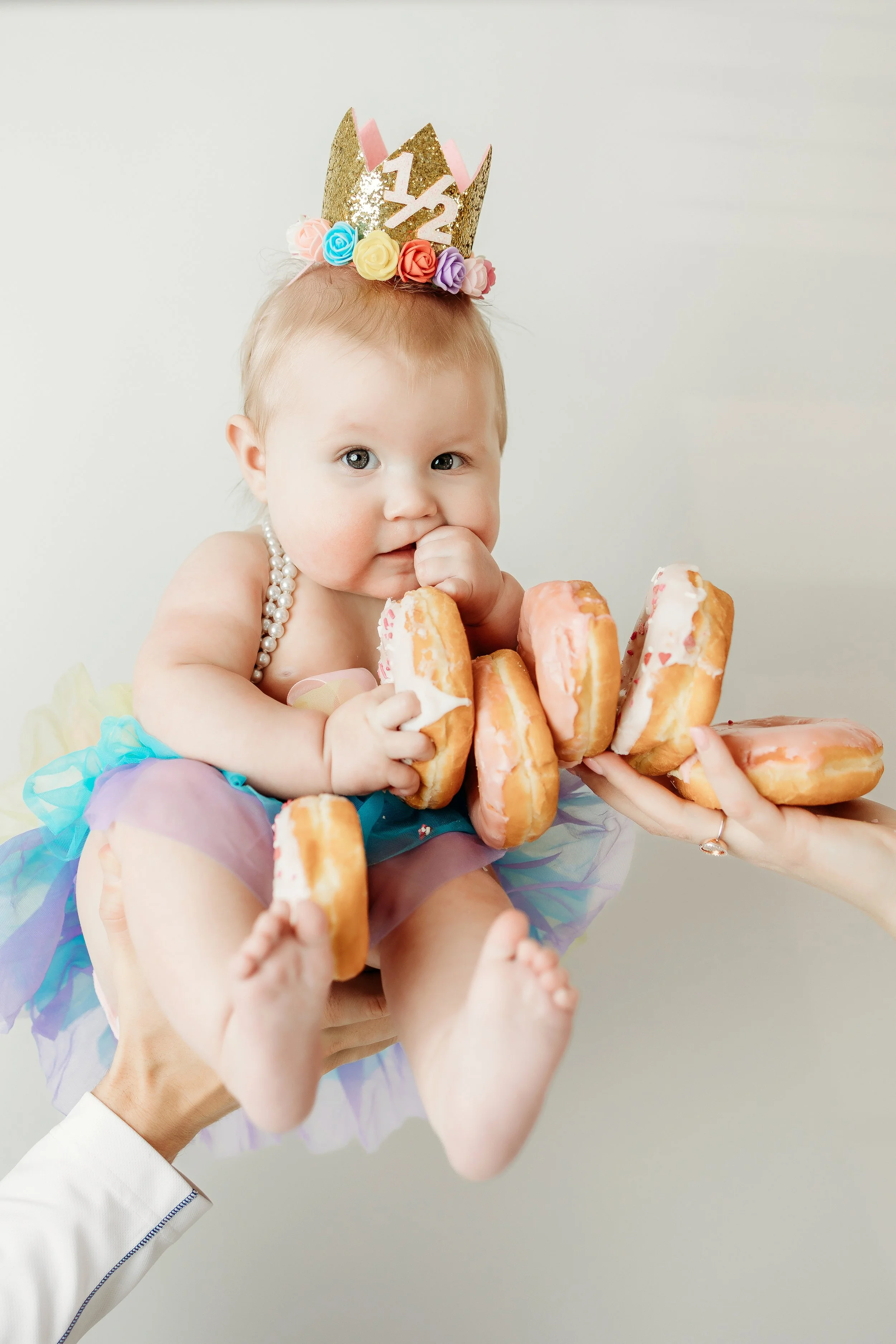 baby in a pink tutu joyfully holds a donut during a 6-month milestone photoshoot.