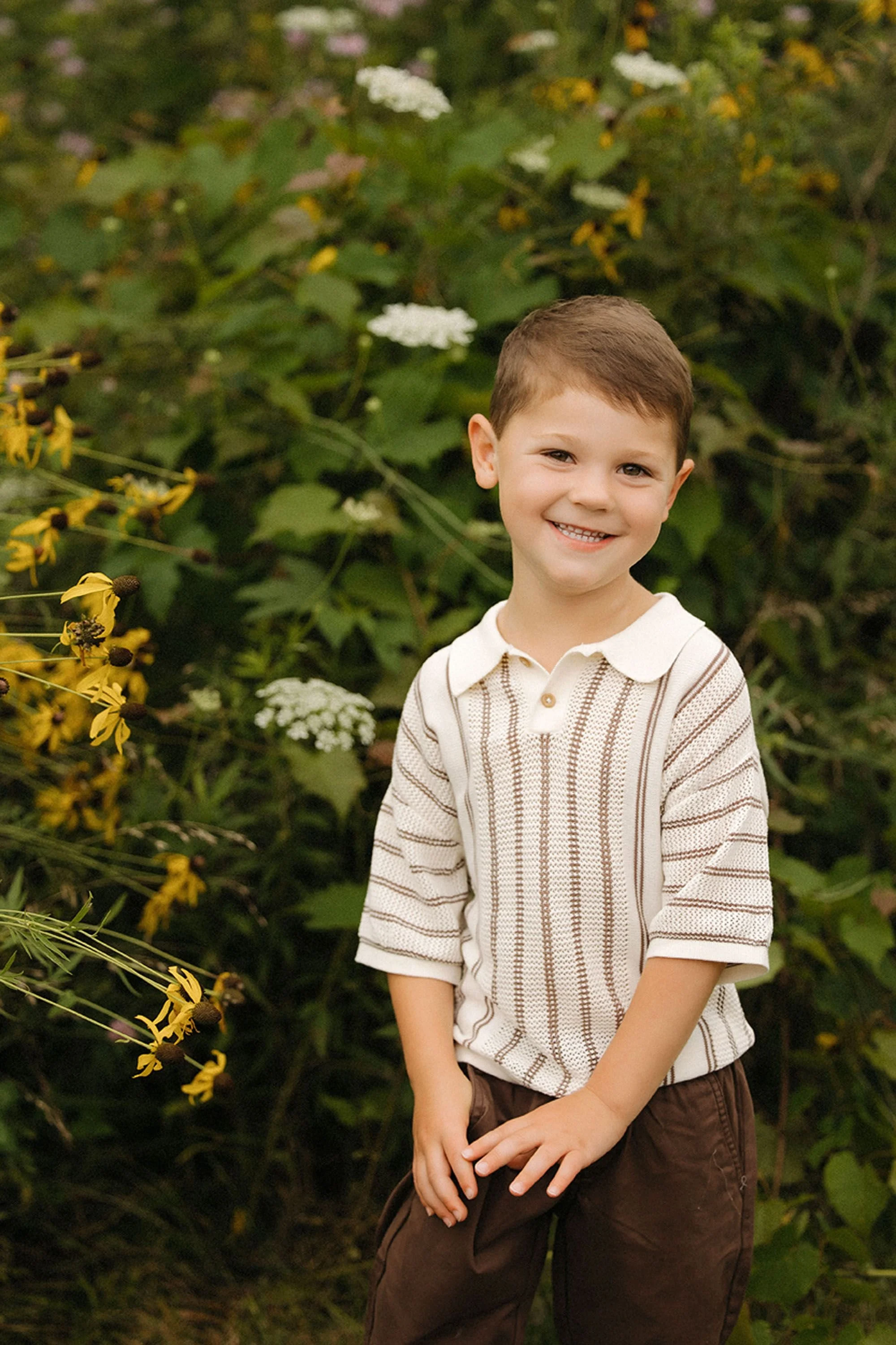 A young boy smiling in a wildflower field during a family photo session at MacGregor Park in Westfield, Indiana.