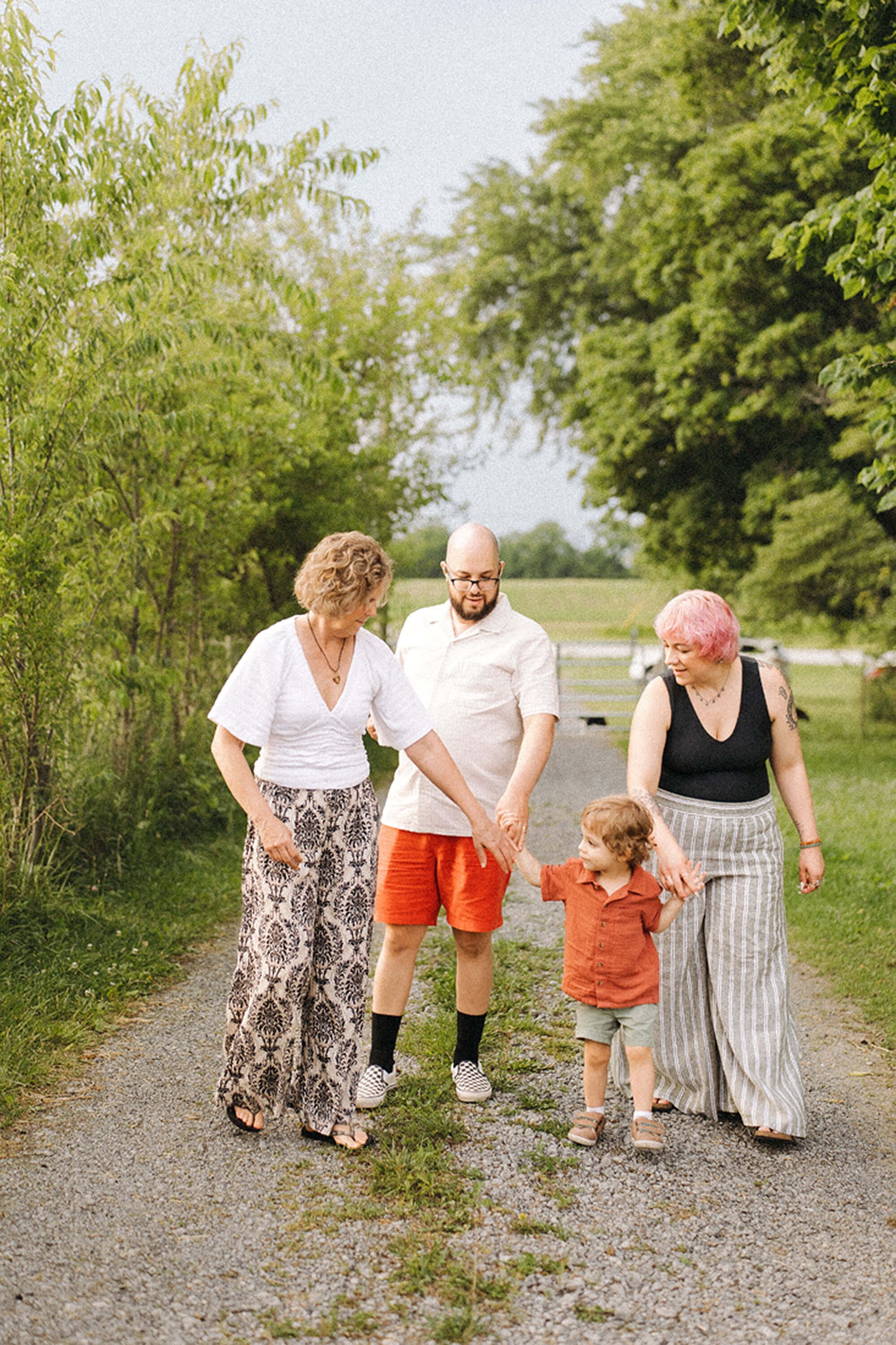 A family walks together along a dirt road at Heavenly Acres Farm, with trees and farmland in the background