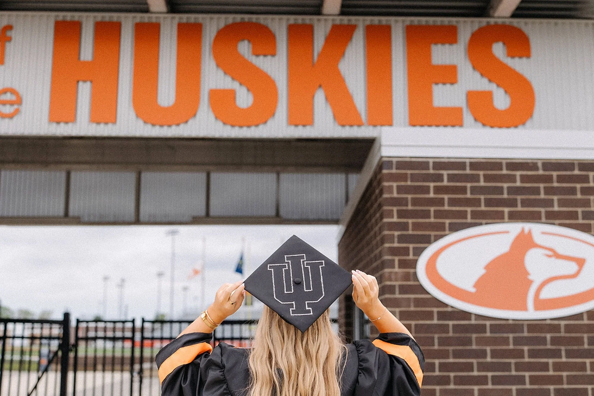 Hamilton Heights Senior Photos featuring a graduating senior in cap and gown showcasing an Indiana University graduation cap design beneath the Hamilton Heights Huskies sign
