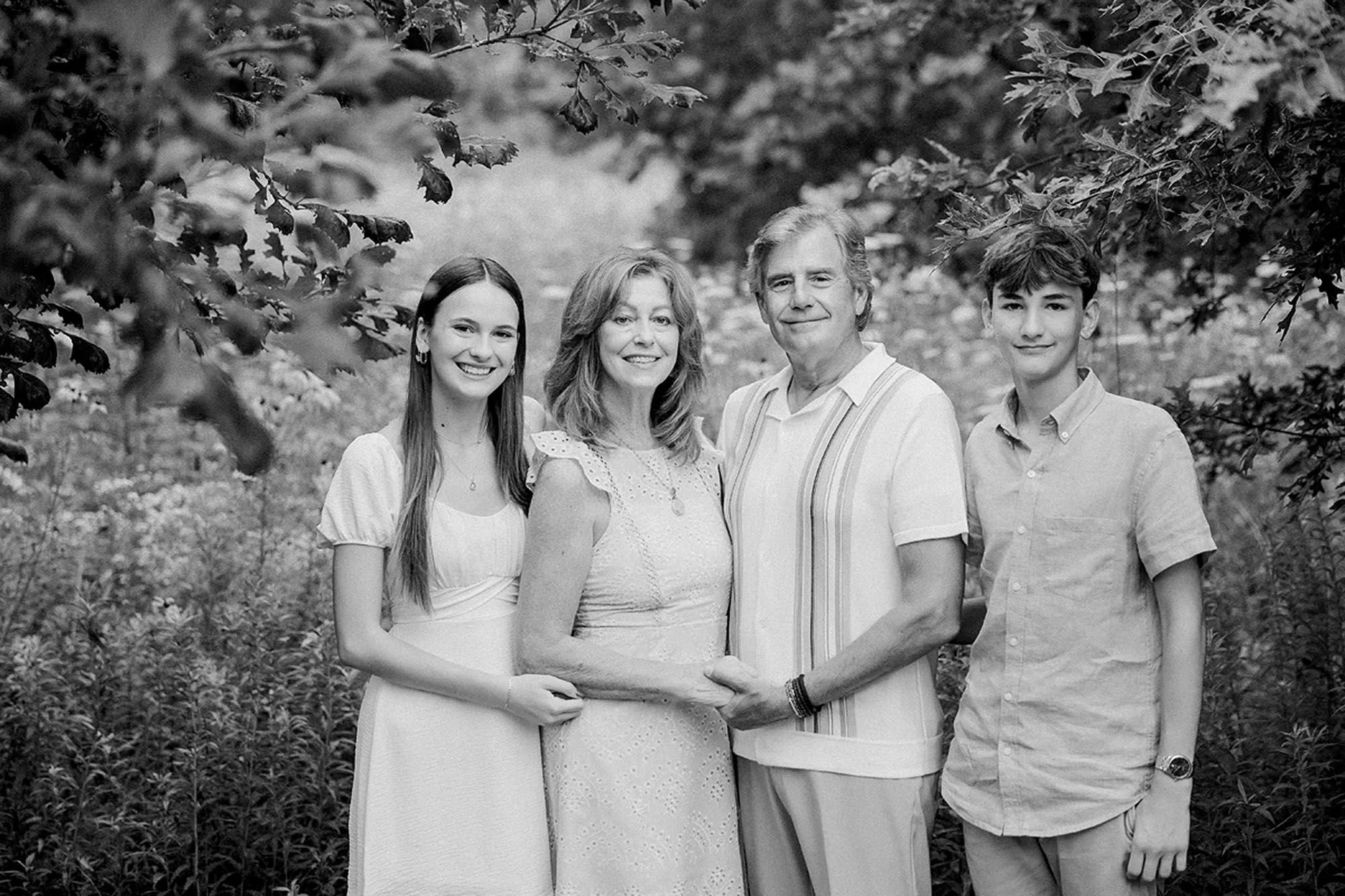 Black and white portrait of a mother, father, and their teenage children together outdoors.