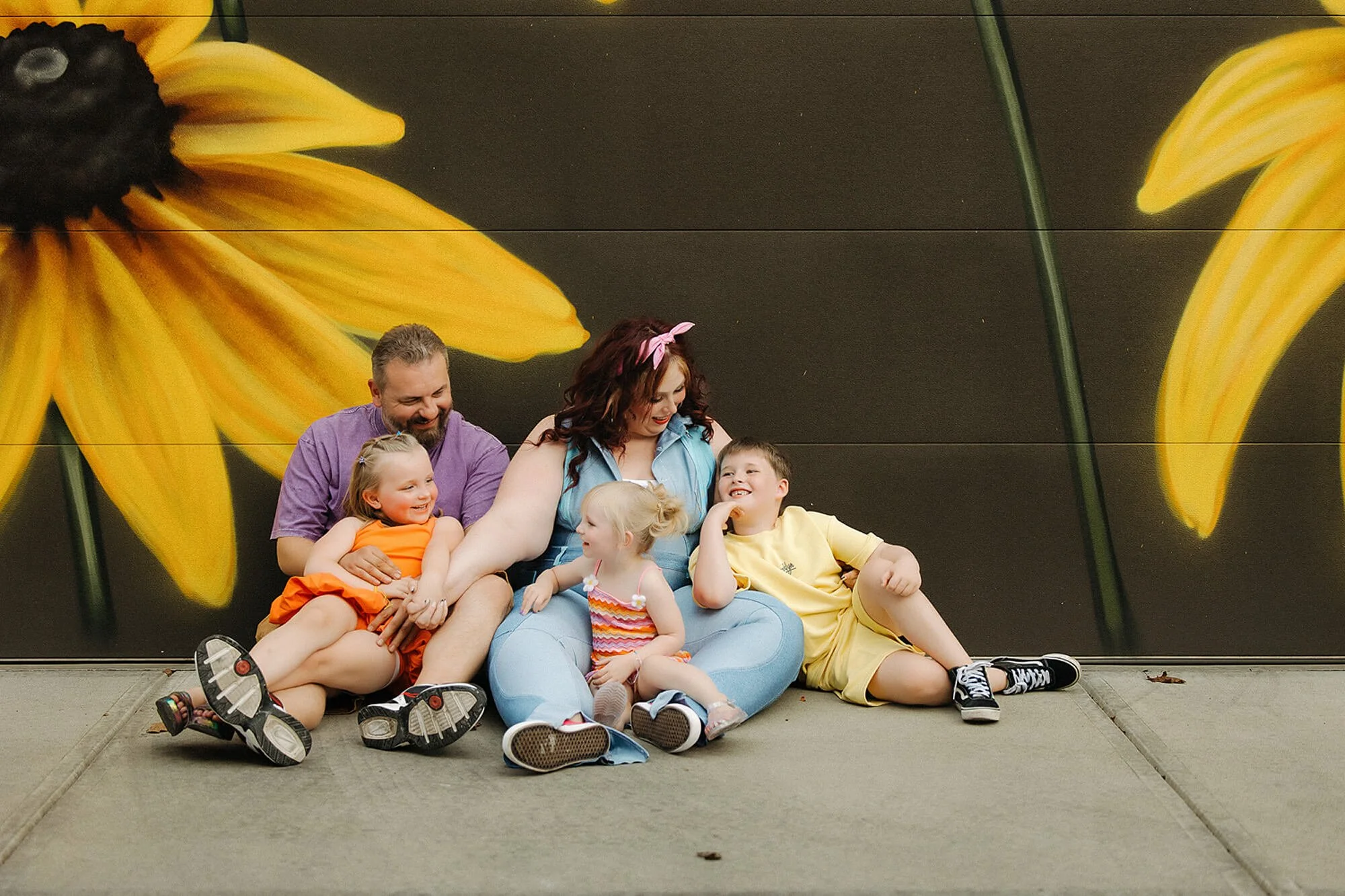 Family of 5 snuggles and laughs together during a family photoshoot at Flower Alley in broadripple in front of flower graffiti- photo by the heart narrative