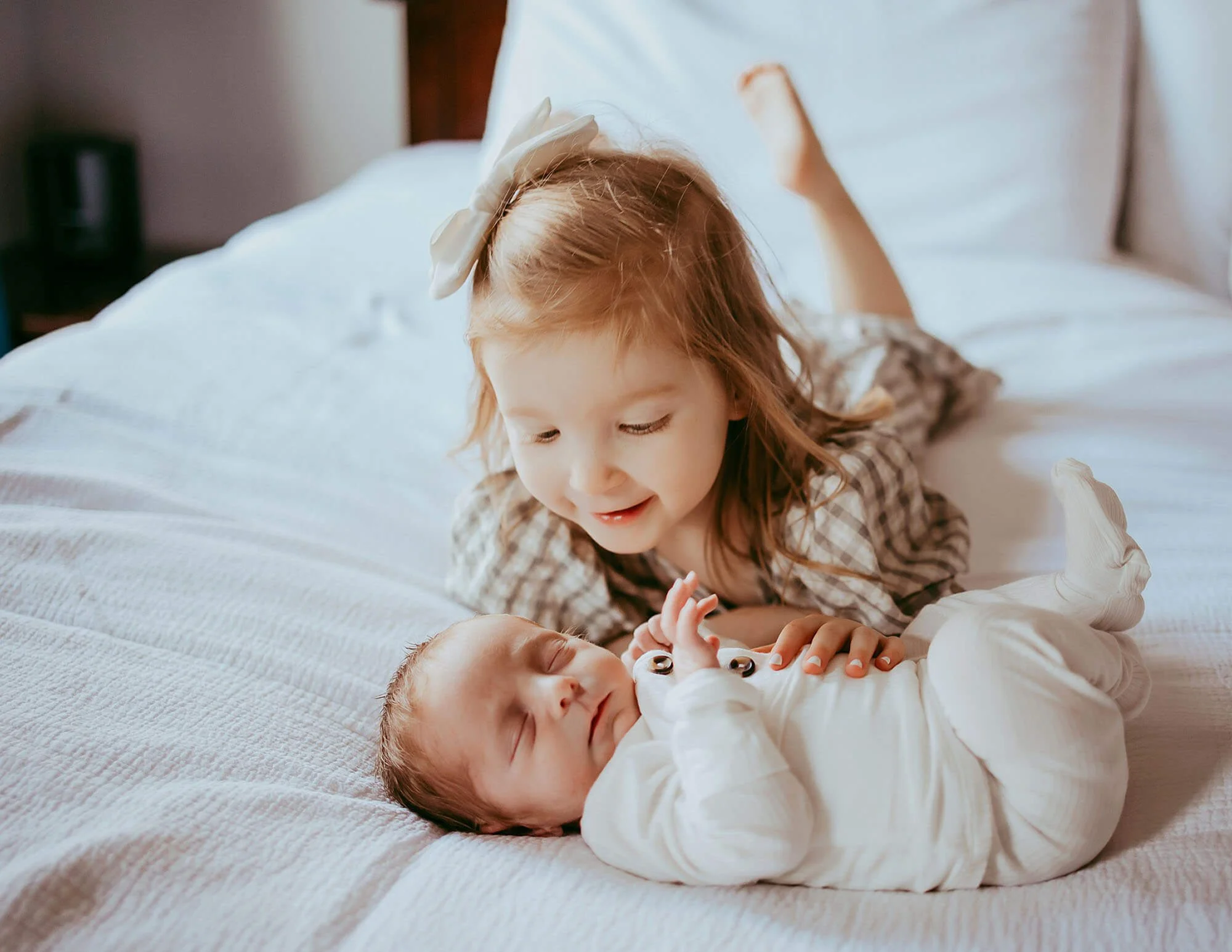 A toddler girl and her baby brother relaxing on a bed, captured during a session for new baby photos