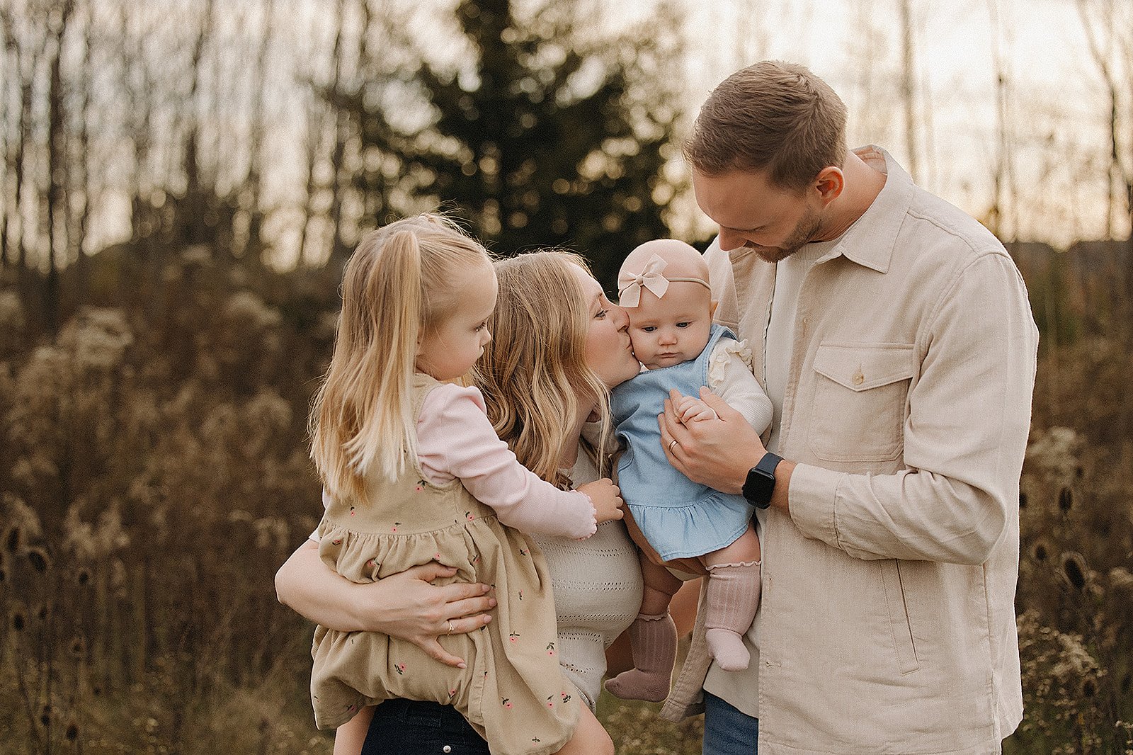 Father holding baby while two young girls smile outdoors at sunset in Indiana.