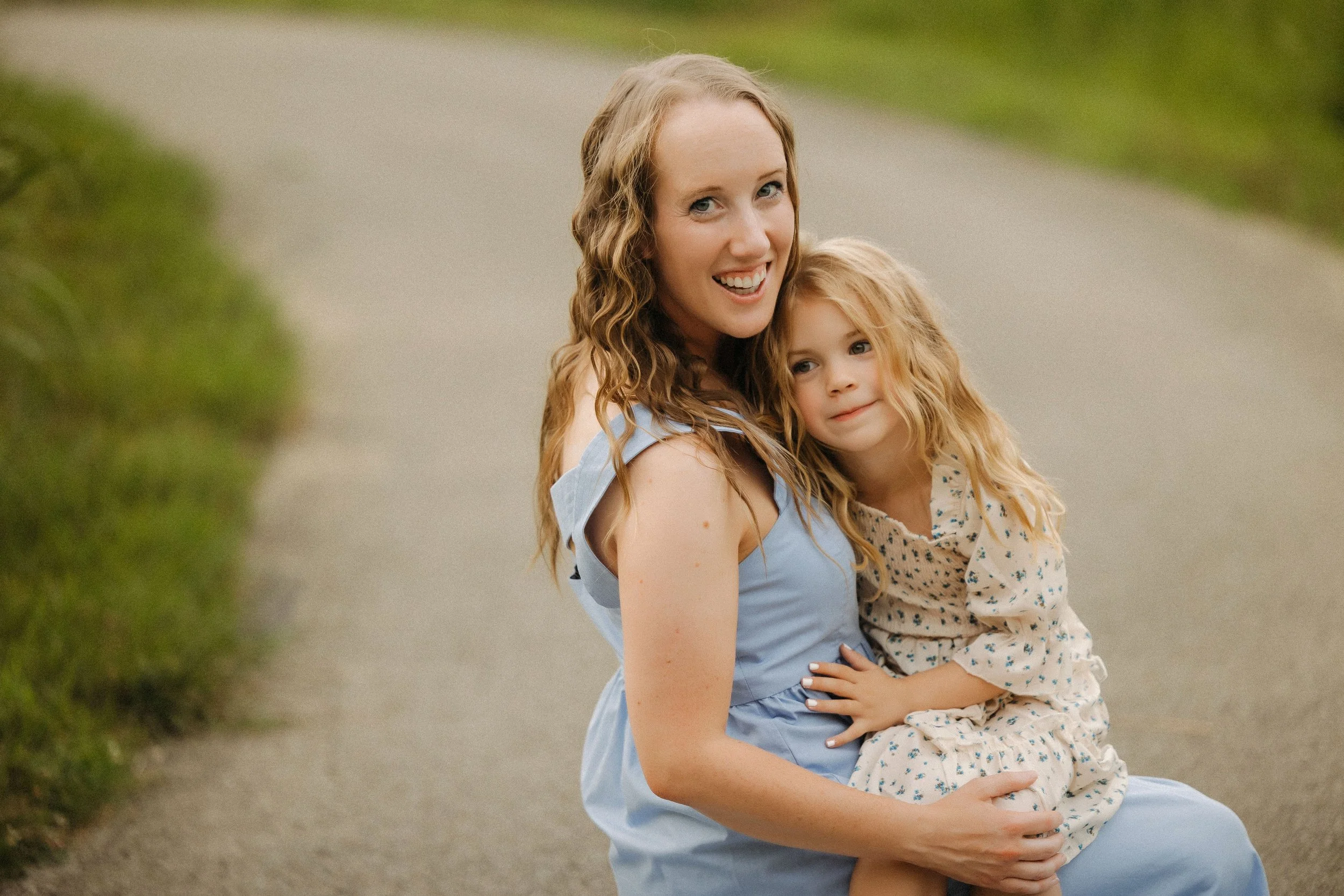 A mother and daughter pose happily on a tranquil country road, capturing a moment of joy in their extended family photo