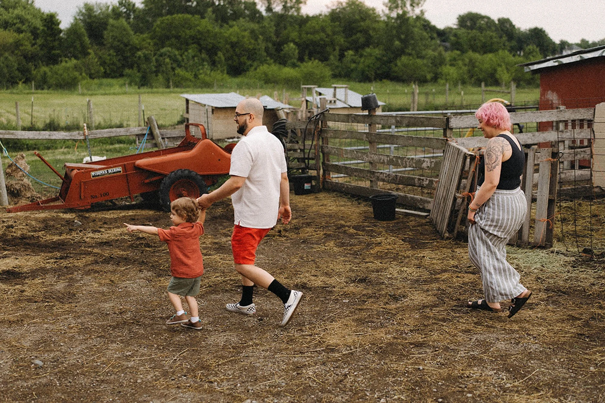 Parents and their young child explore the open grounds of Heavenly Acres Farm, discovering the sights and charm of a peaceful family farm