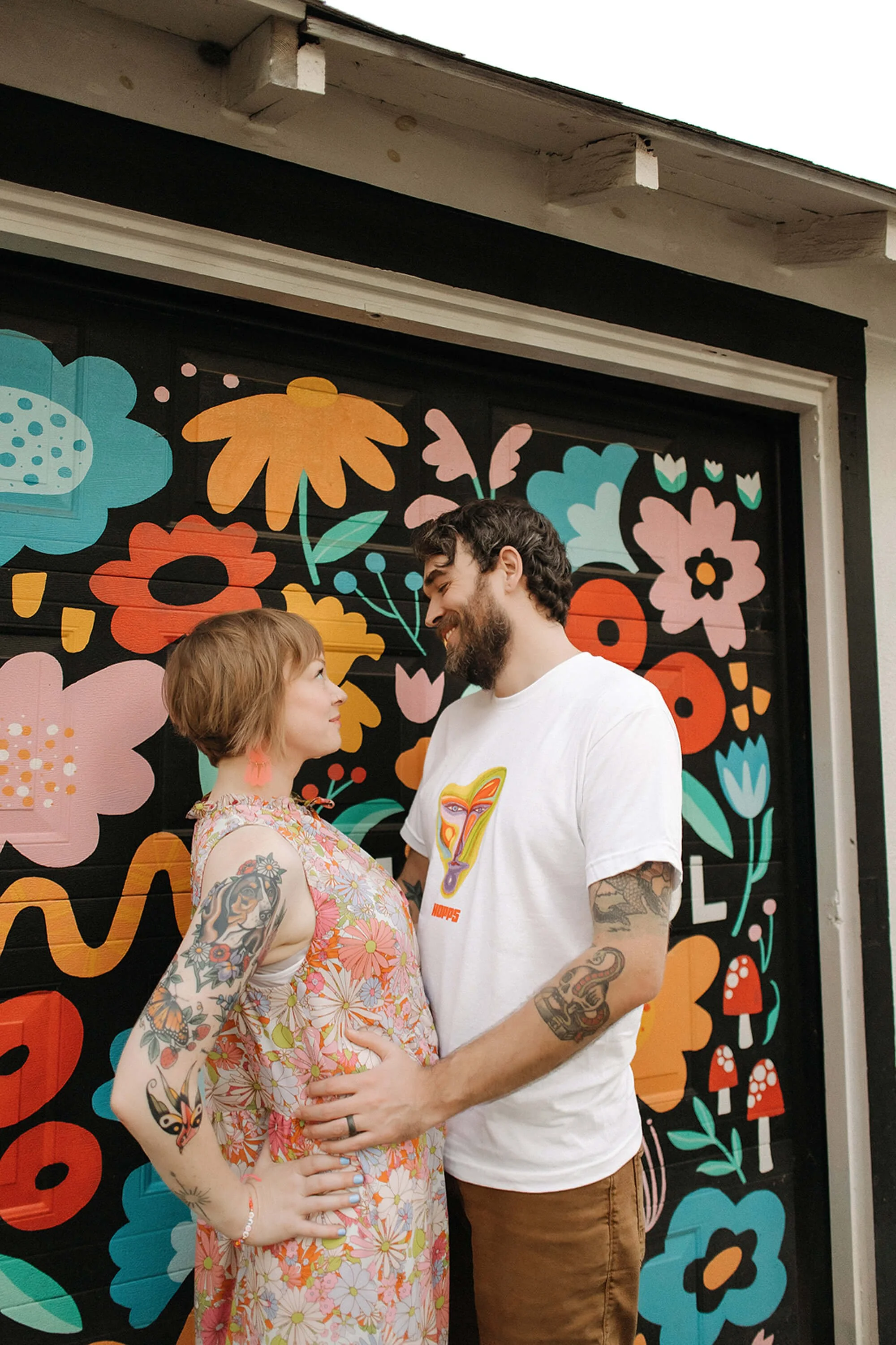  couple stands together in 90’s vintage outfits in front of flower alley in broadripple indiana during unique family photoshoot with the heart narrative 