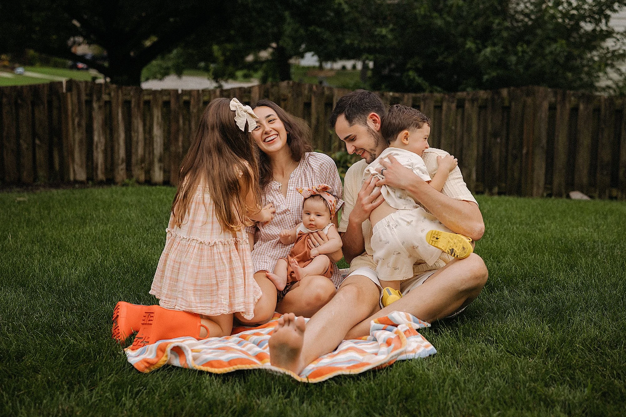 Family of 5 plays and laughs together while sitting on a family quilt in the backyard of their noblesville home