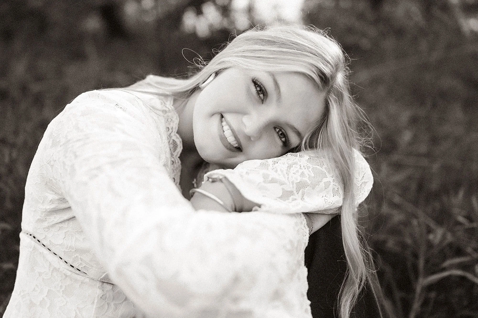 Smiling high school senior in a white lace dress during a natural outdoor senior photos session with timeless black and white portrait styling