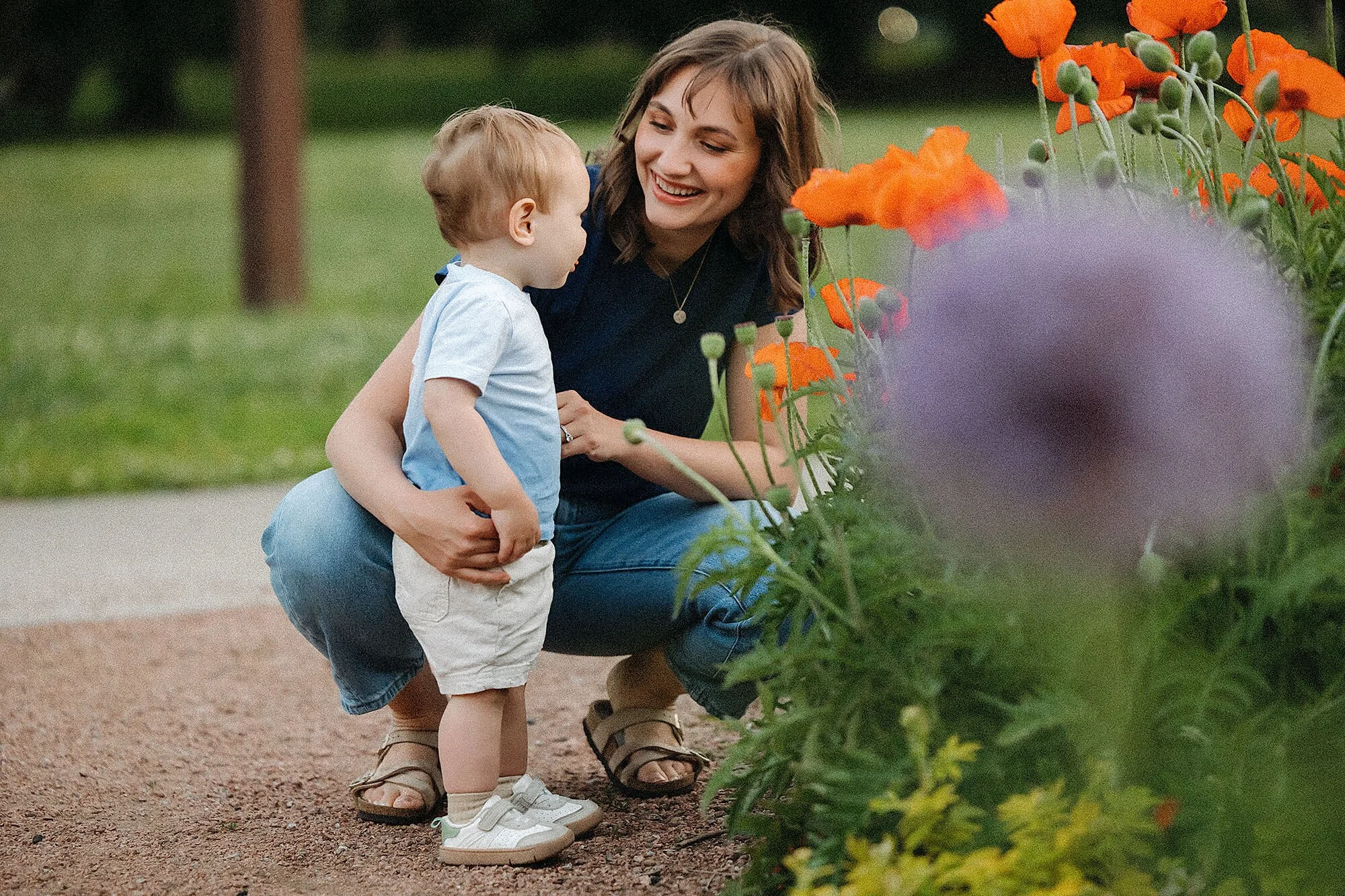 Mom hugging her toddler son while looking at orange and purple flowers during a candid family mini session.