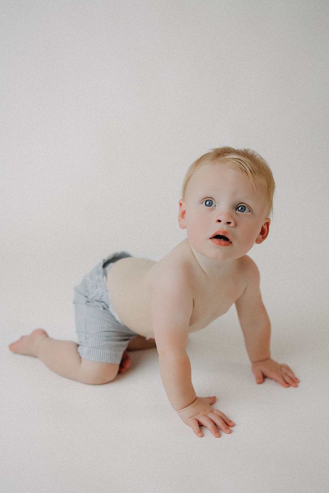 A baby with light skin at a crawling position, wearing only striped shorts, on a plain white background.