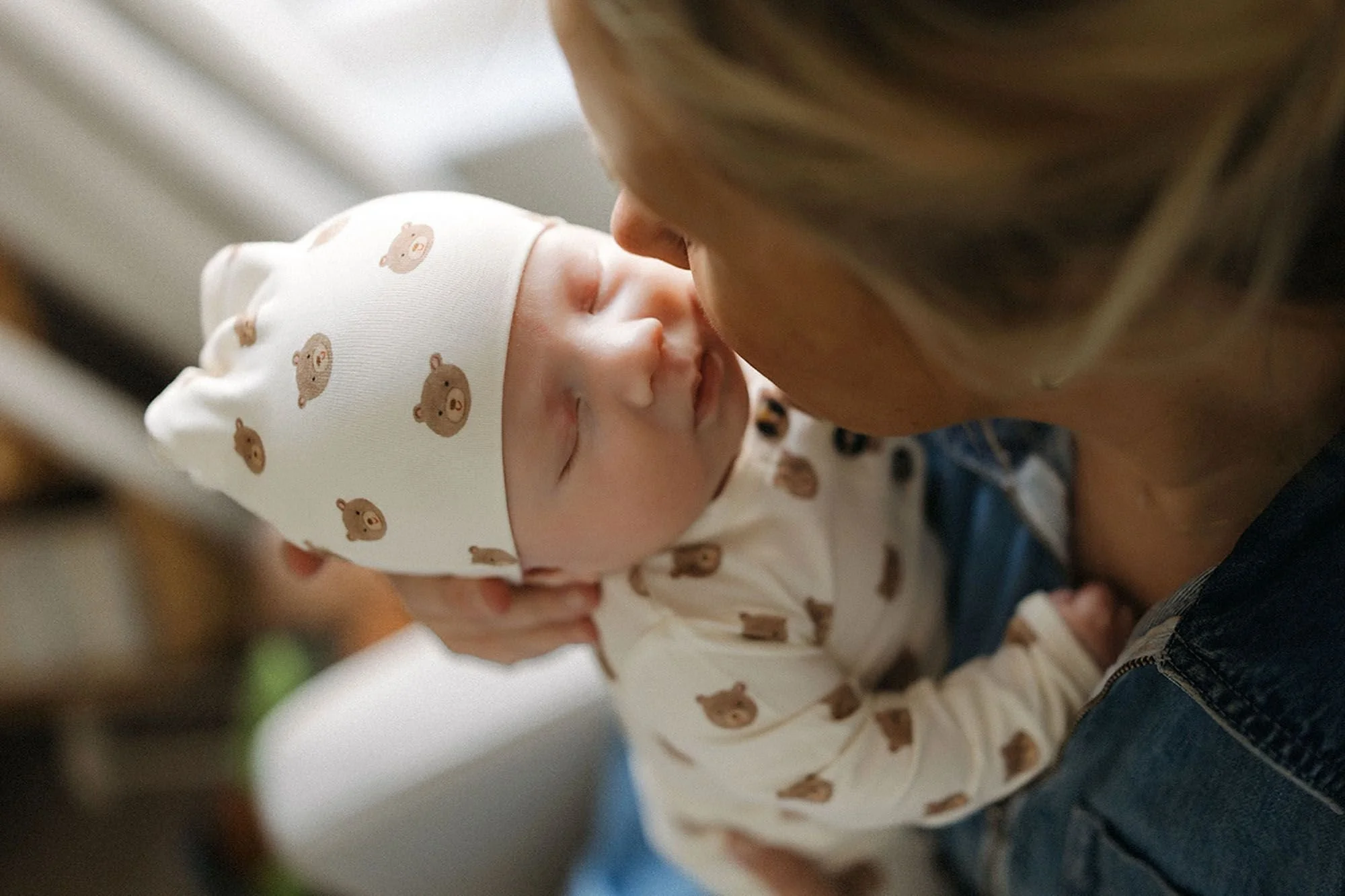 Pro Tips for Newborn Photos with Siblings – Parent gently kisses a sleeping newborn baby while holding them close during a warm, intimate in-home lifestyle photography session