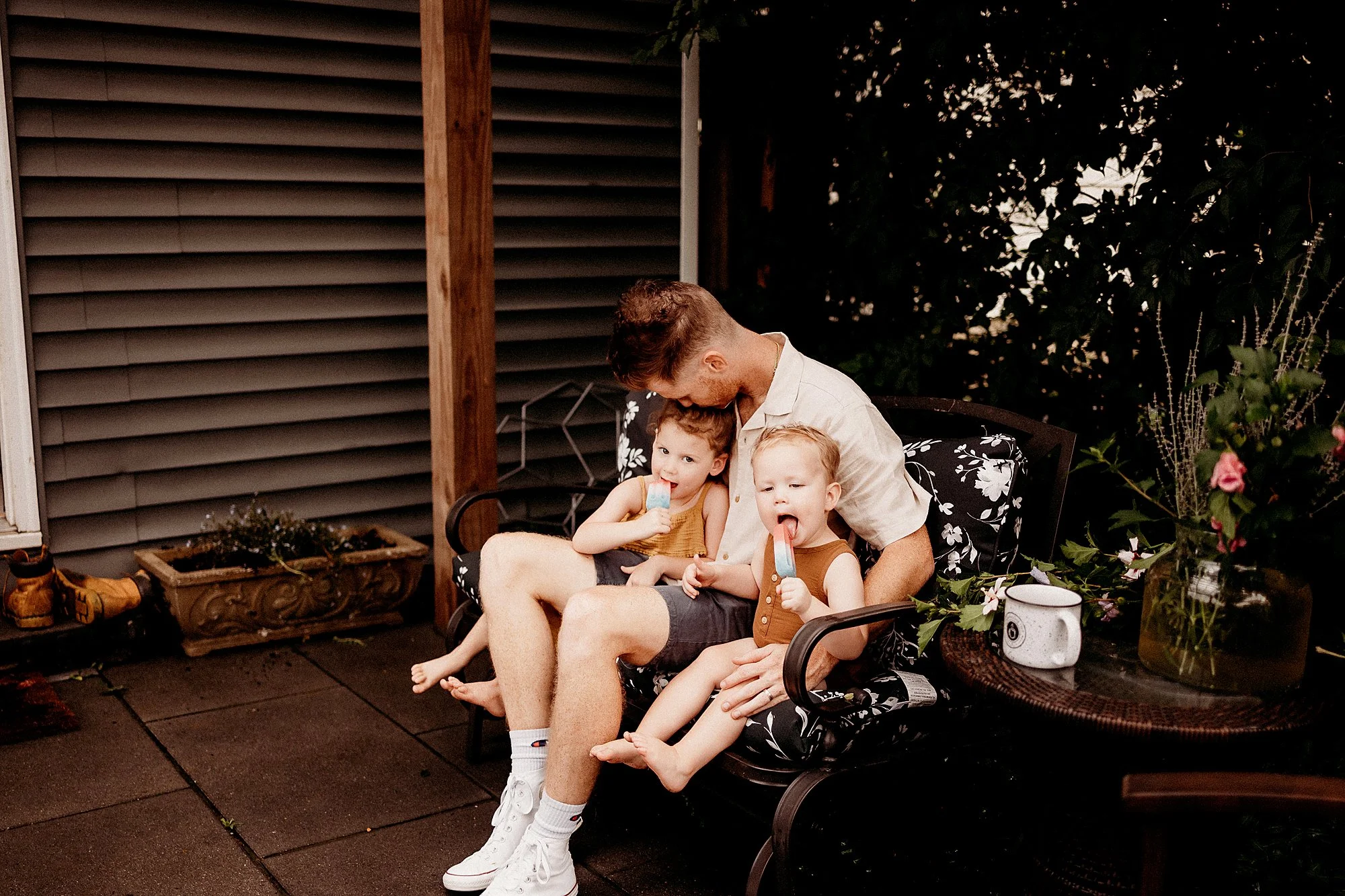 A Father and two children relax together on a patio during a backyard photography session in Indianapolis, Indiana