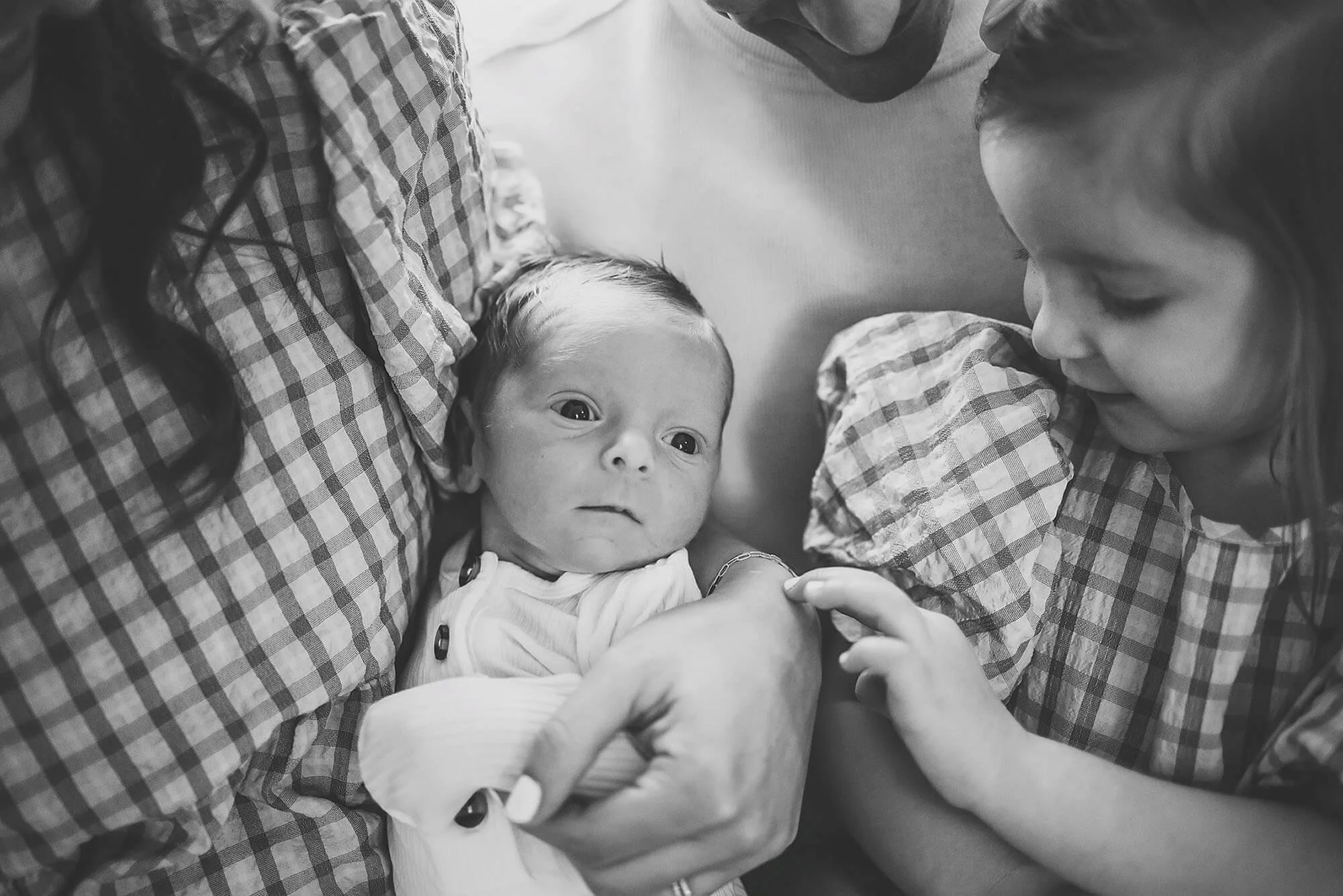 A black and white photograph featuring a family proudly holding their baby, taken during a New Baby Photos session