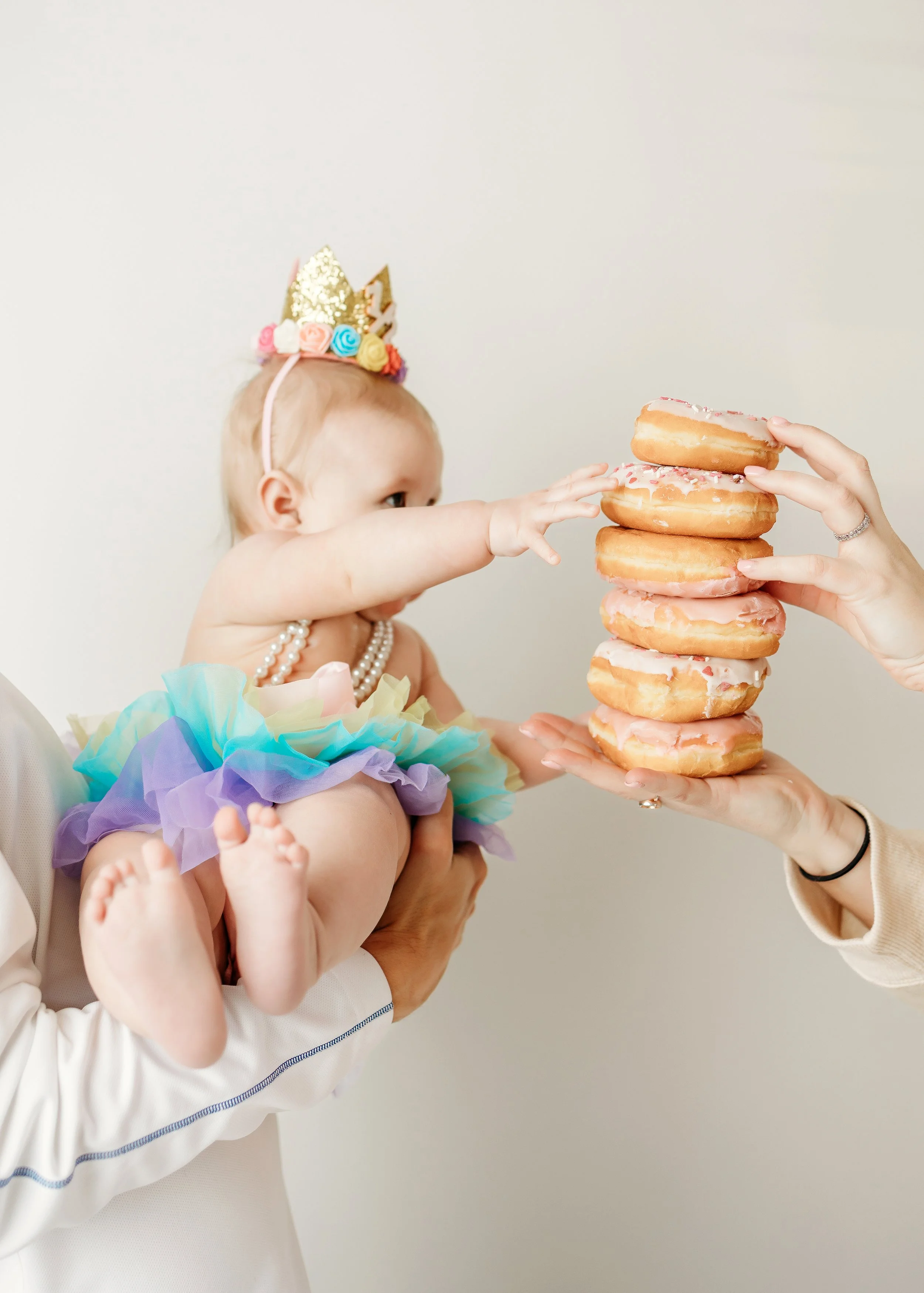 A baby joyfully holds a colorful stack of donuts during a 6-month milestone photoshoot