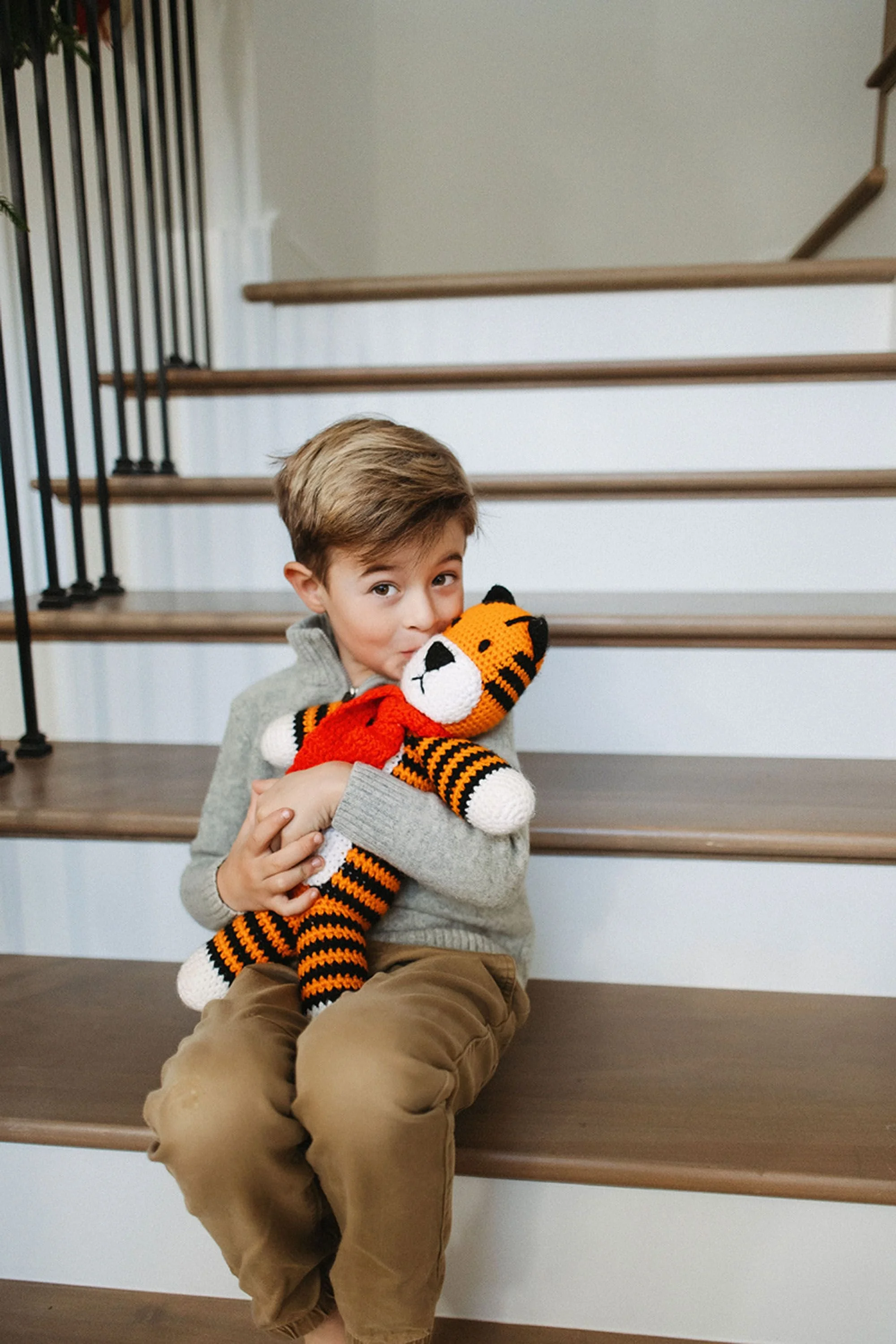 A sweet holiday moment of a young boy cuddling a festive tiger stuffed toy on the stairs, capturing the warmth and playful charm of Christmas pictures in Chatham Hills.