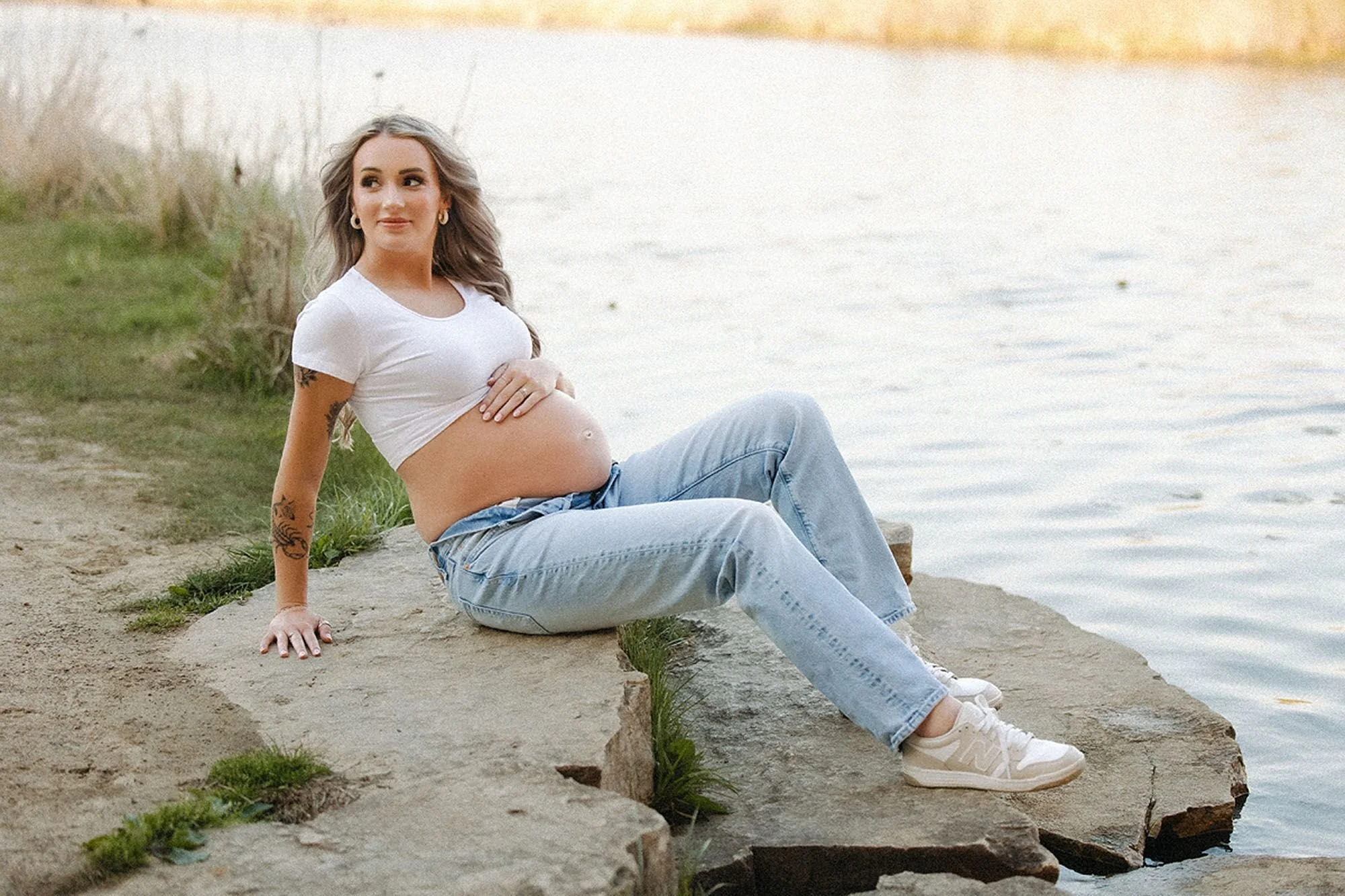 Expectant mother posing by the water in a white top and relaxed denim, modern Maternity Photos in Central Indiana