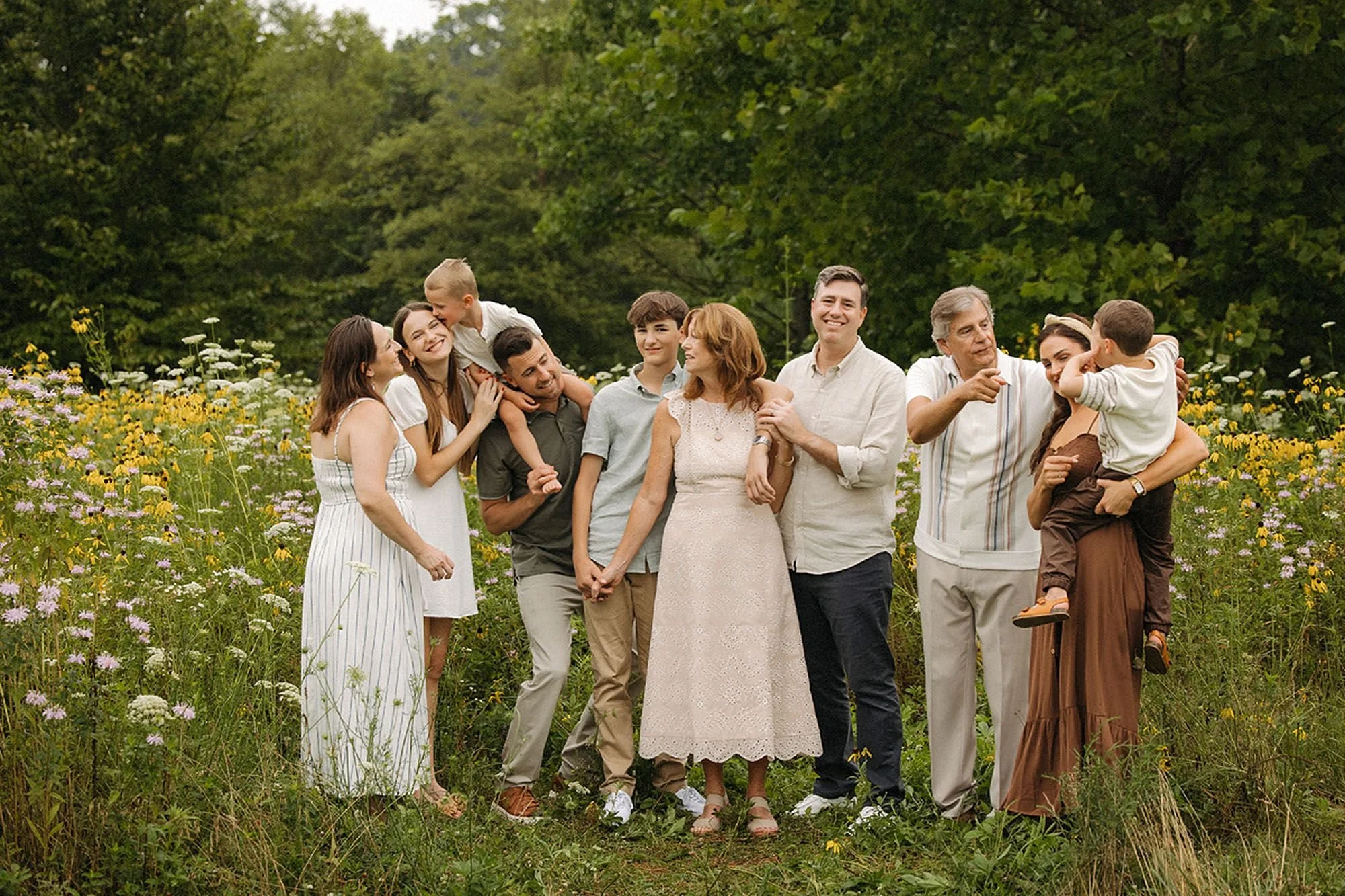 Extended family embracing and laughing together in a wildflower field during a summer session in Westfield, Indiana.