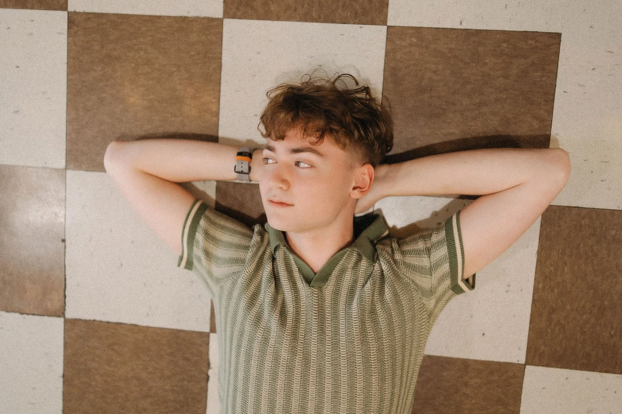 Senior photo of a man reclining on a checkered floor in Fountain Square, Indianapolis, arms extended upward