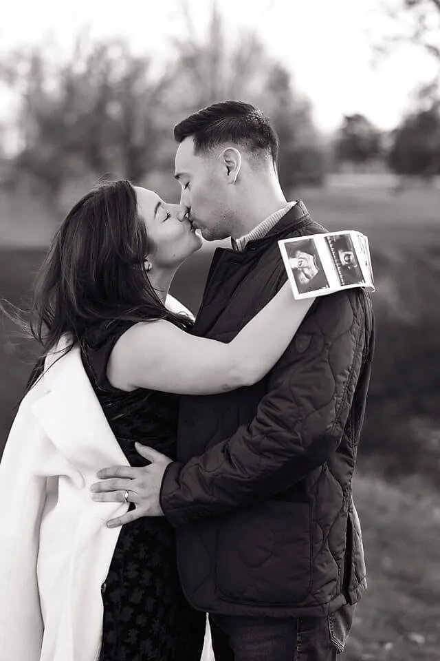 Golden Hour Fall Pregnancy Announcement Photos capturing an intimate kiss between an expecting couple, with a tiny ultrasound print resting on his shoulder as they celebrate their growing family.