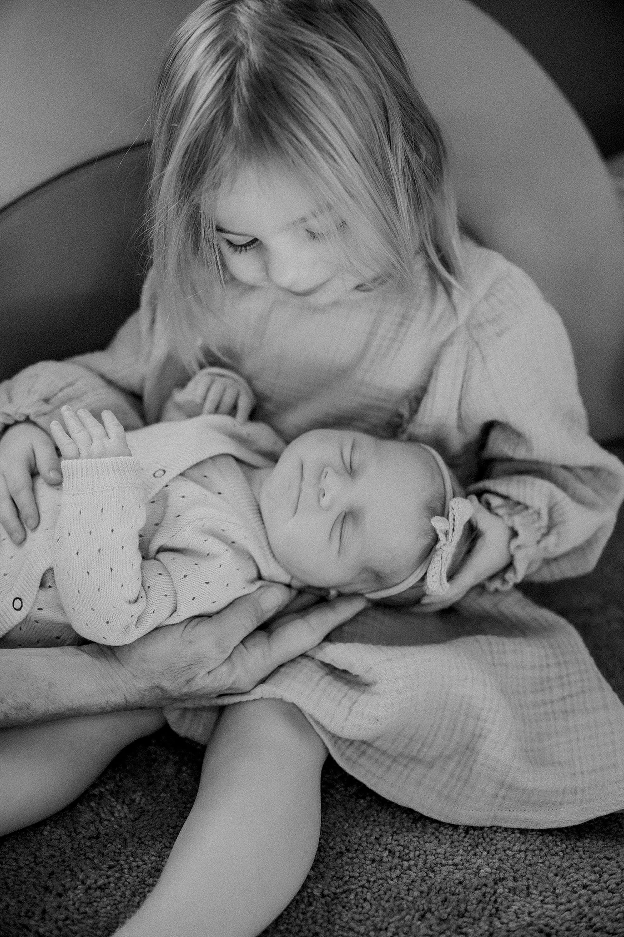black and white photo of a toddler sibling leaning in close to newborn baby