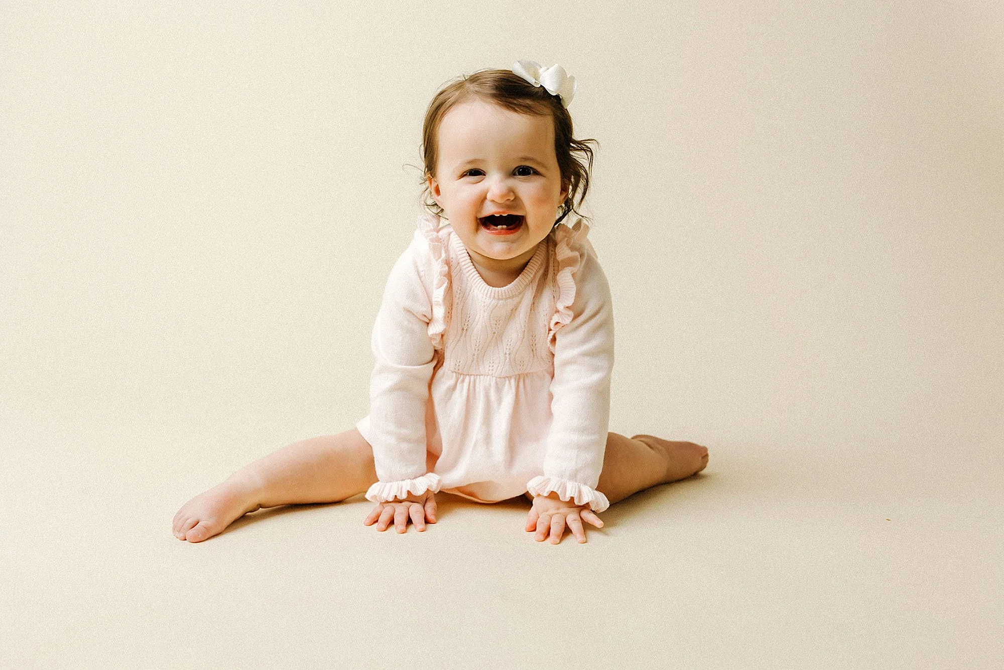 A baby girl sitting on the floor, laughing and celebrating her first birthday Milestone during a photography session in Westfield, Indiana