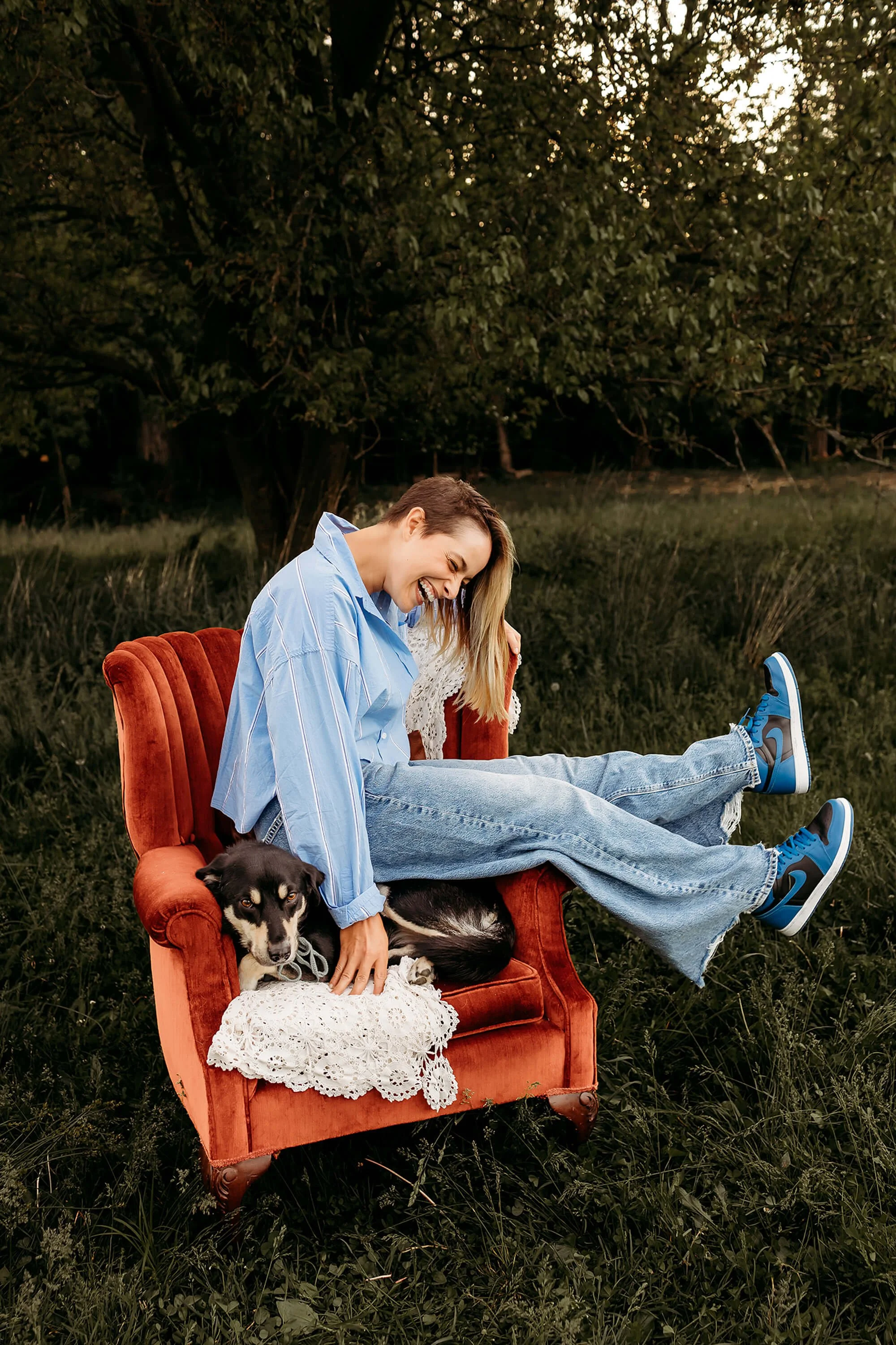 A woman in spring attire sits on a chair with a dog beside her, enjoying a sunny day outdoors