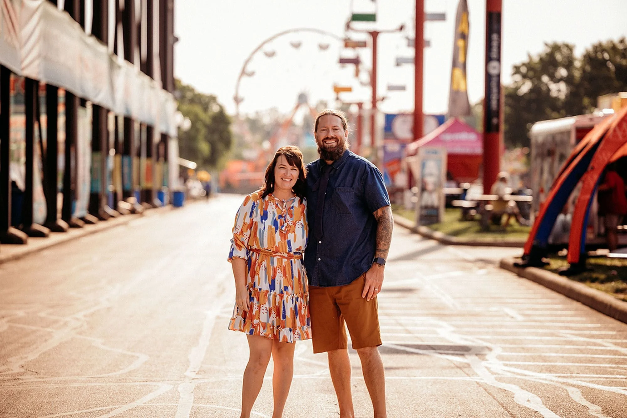 A couple enjoys a fun day at an Indiana carnival, posing in front of a vibrant ferris wheel illuminated by lights