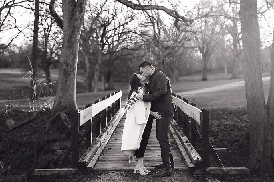 Romantic Pregnancy Announcement Photos of an expecting couple sharing a tender kiss on a wooden bridge in a peaceful fall setting
