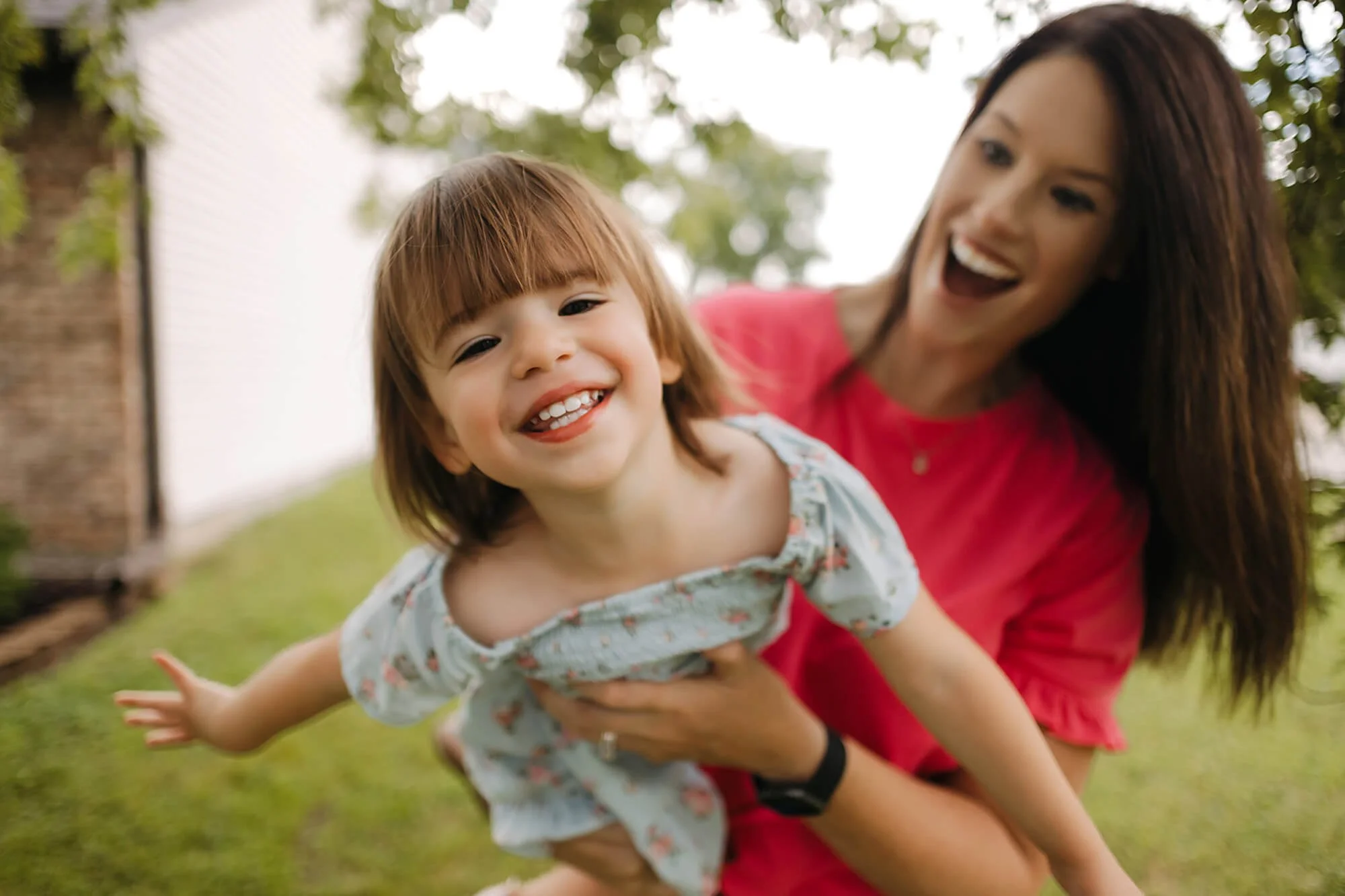 A joyful toddler smiles while being lifted by her mother during an in-home family photography session in Fishers, Indiana