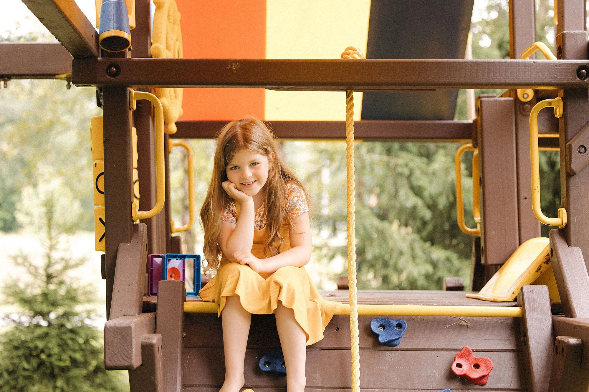 Girl in yellow dress smiles from her backyard swingset during documentary at home family photoshoot with the heart narrative