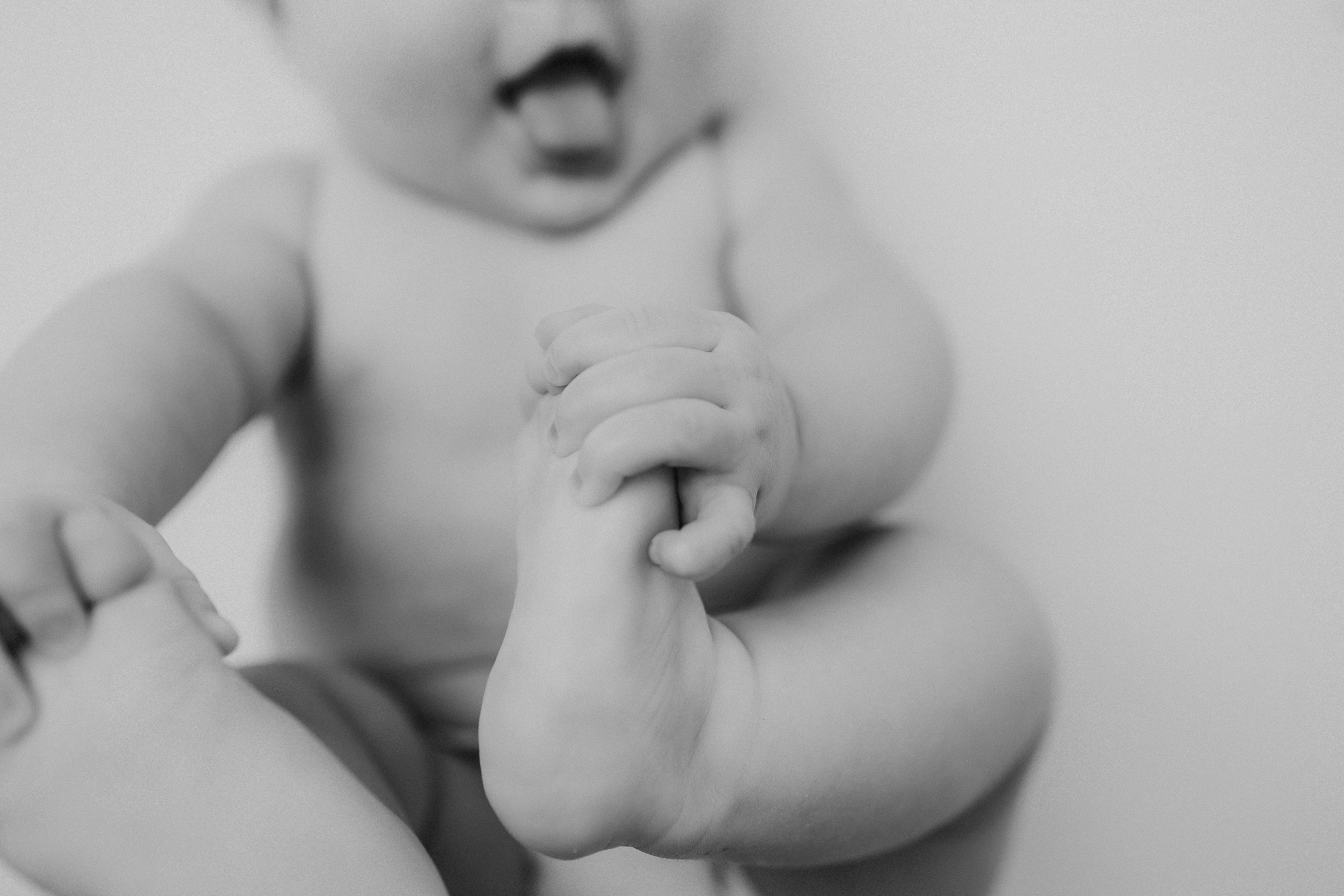 A baby sits on the floor with feet raised, looking playful and curious.