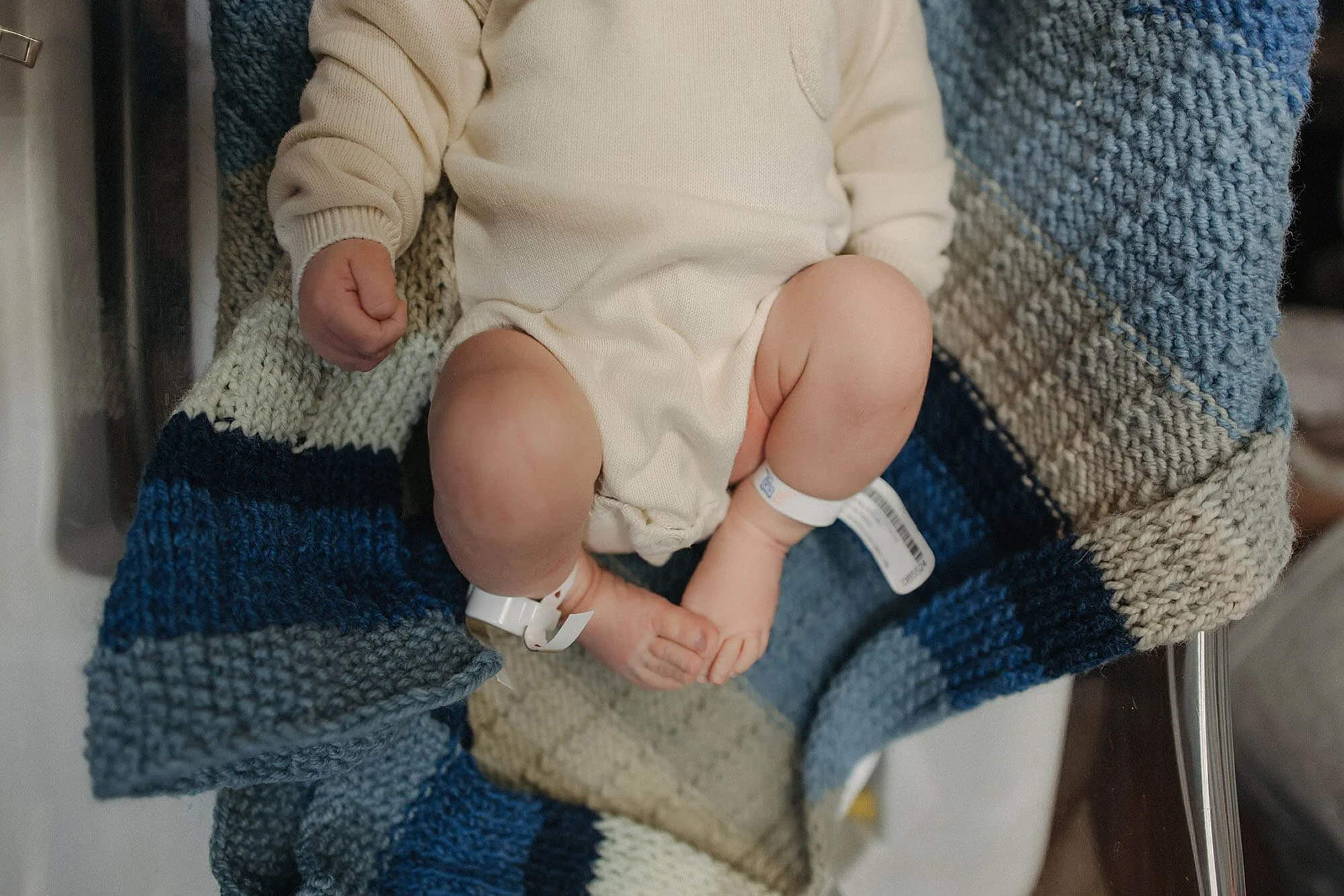 Newborn baby in a white onesie, wrapped in a soft blue blanket, captured during a Fresh 48 hospital photo session