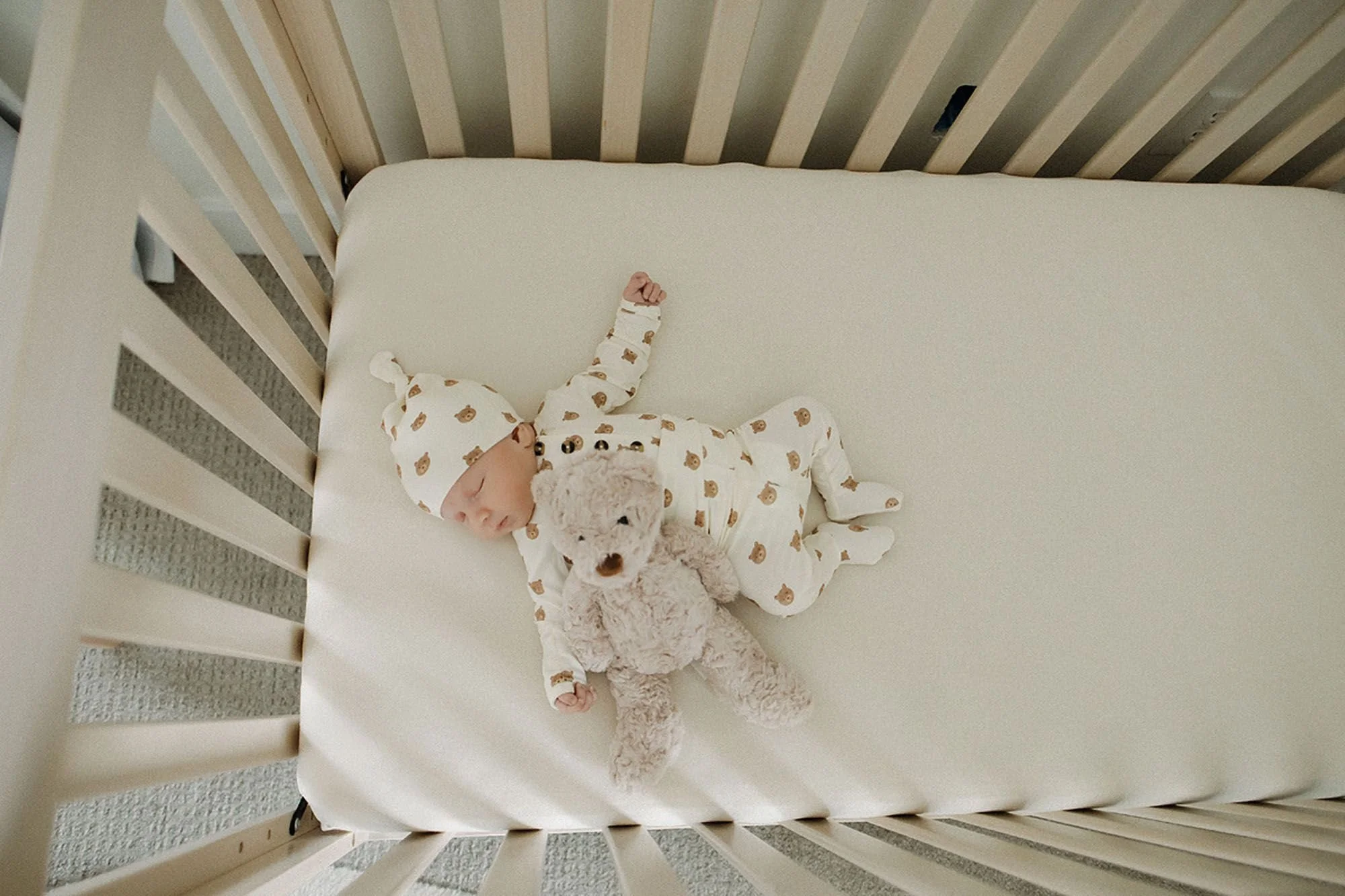 Peaceful newborn baby sleeping in a cozy crib with a soft teddy bear, dressed in a neutral bear-print outfit, capturing a calm nursery moment with timeless lifestyle newborn photography and safe sleep inspiration