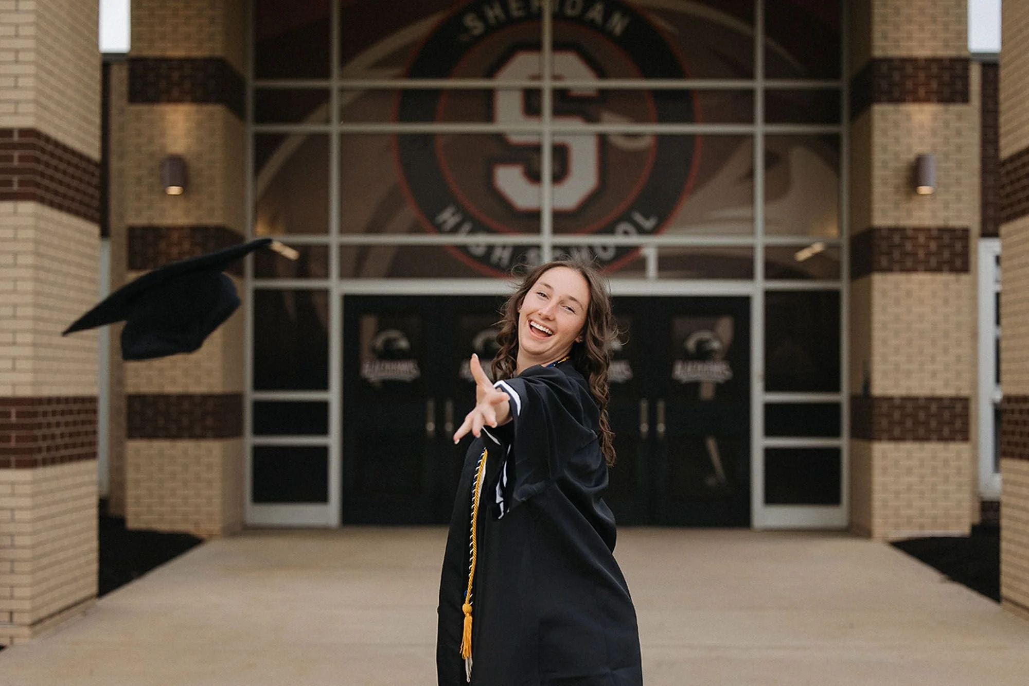 Sheridan High School senior photos featuring a joyful graduate in her cap and gown, celebrating her achievement on campus with a bright, natural smile